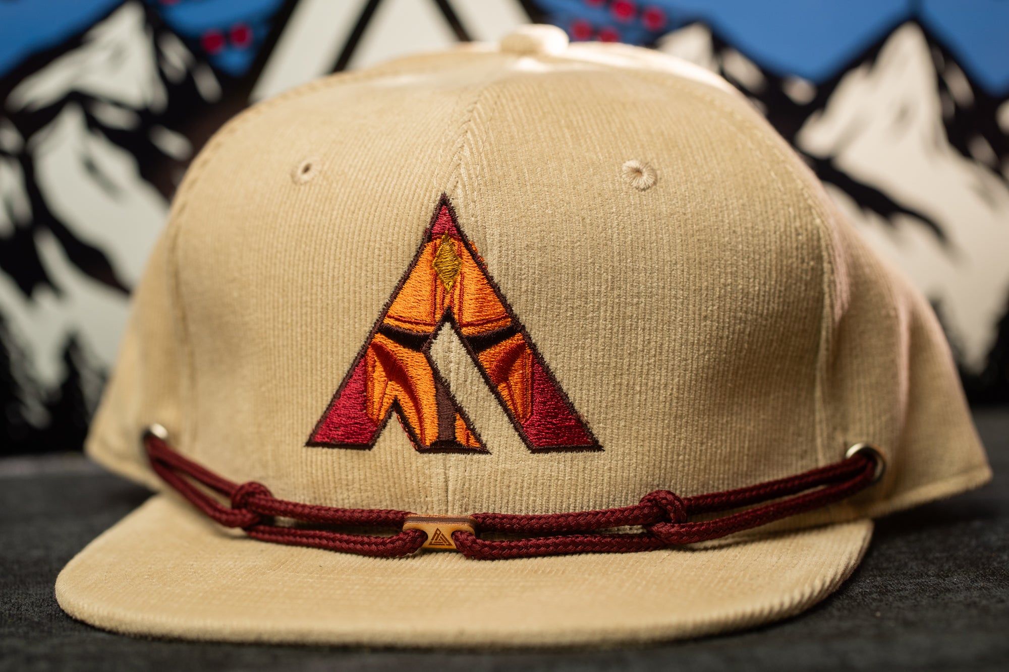 A beige baseball cap with a red and orange embroidered logo on the front.