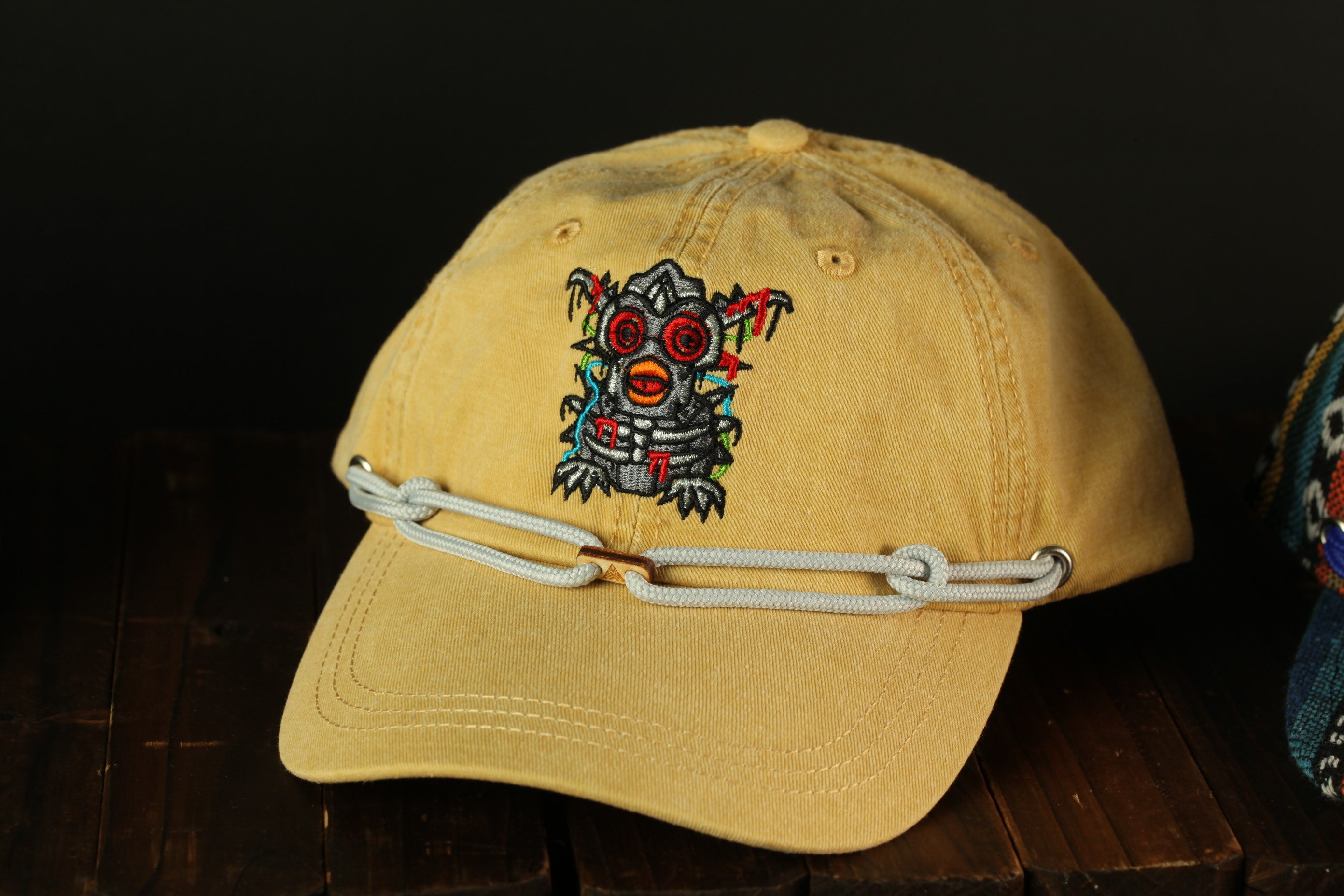 A yellow baseball cap with a colorful, embroidered design on the front, featuring a character-like figure with red eyes and a red mouth.
