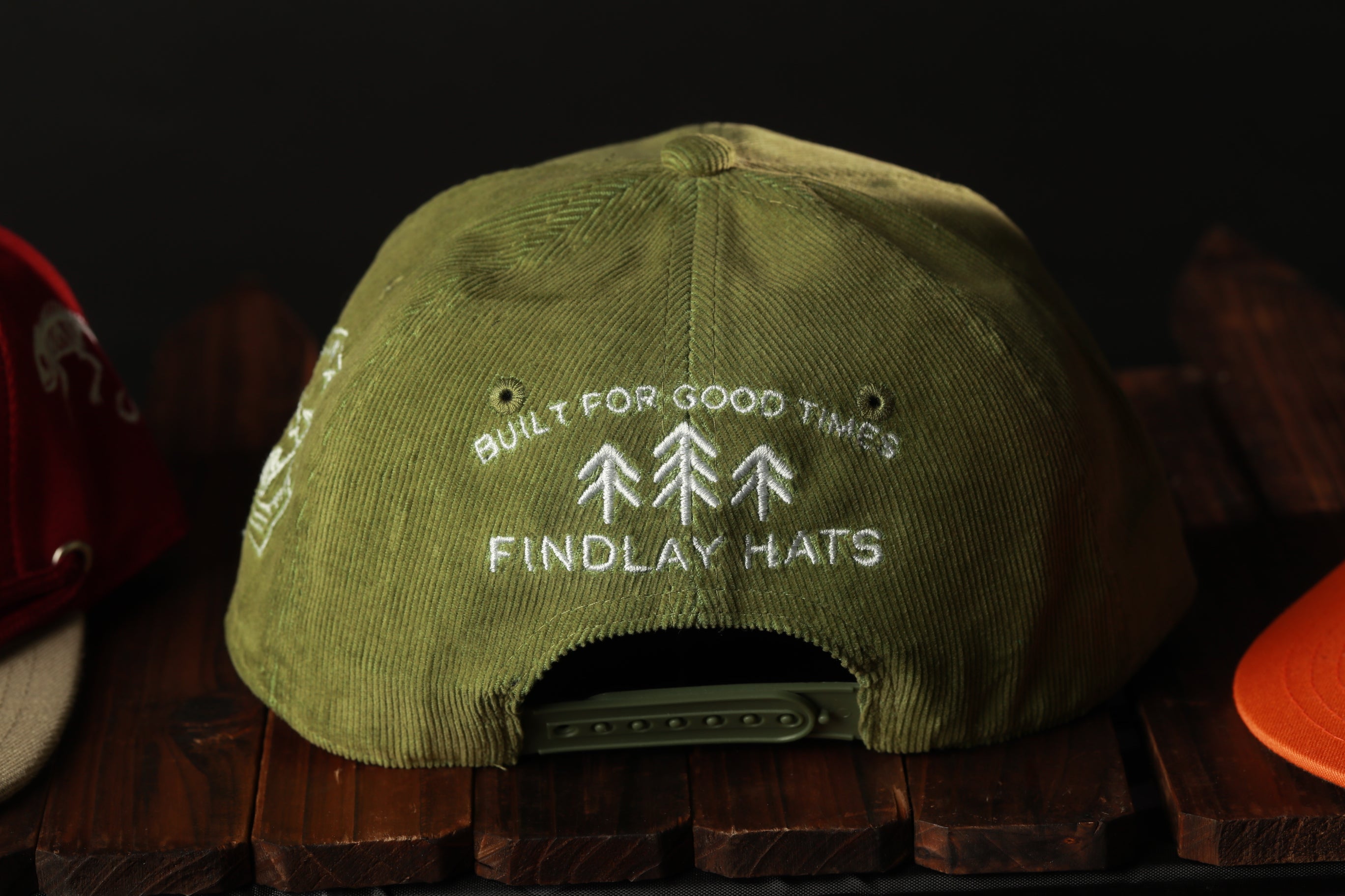 A green baseball cap with white text on it, sitting on a wooden surface.