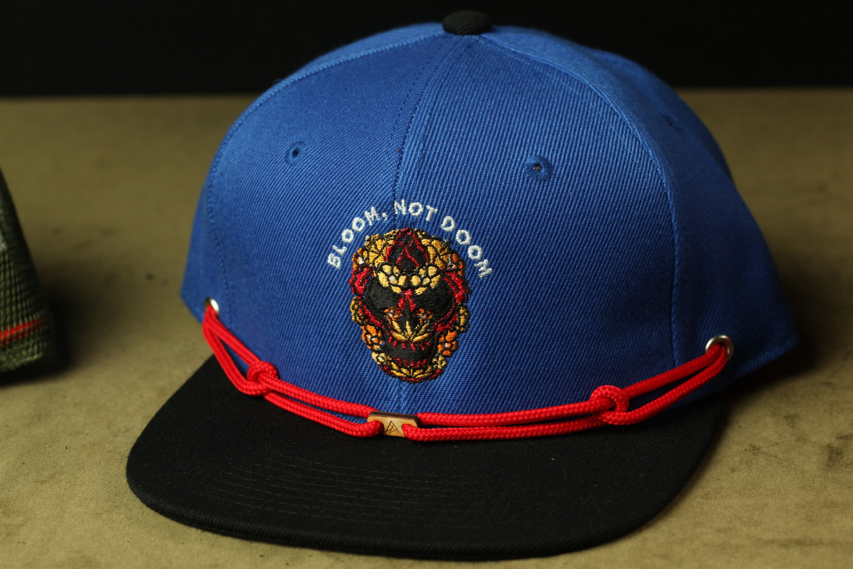 A blue baseball cap with a red string and a black brim, featuring an embroidered design on the front.