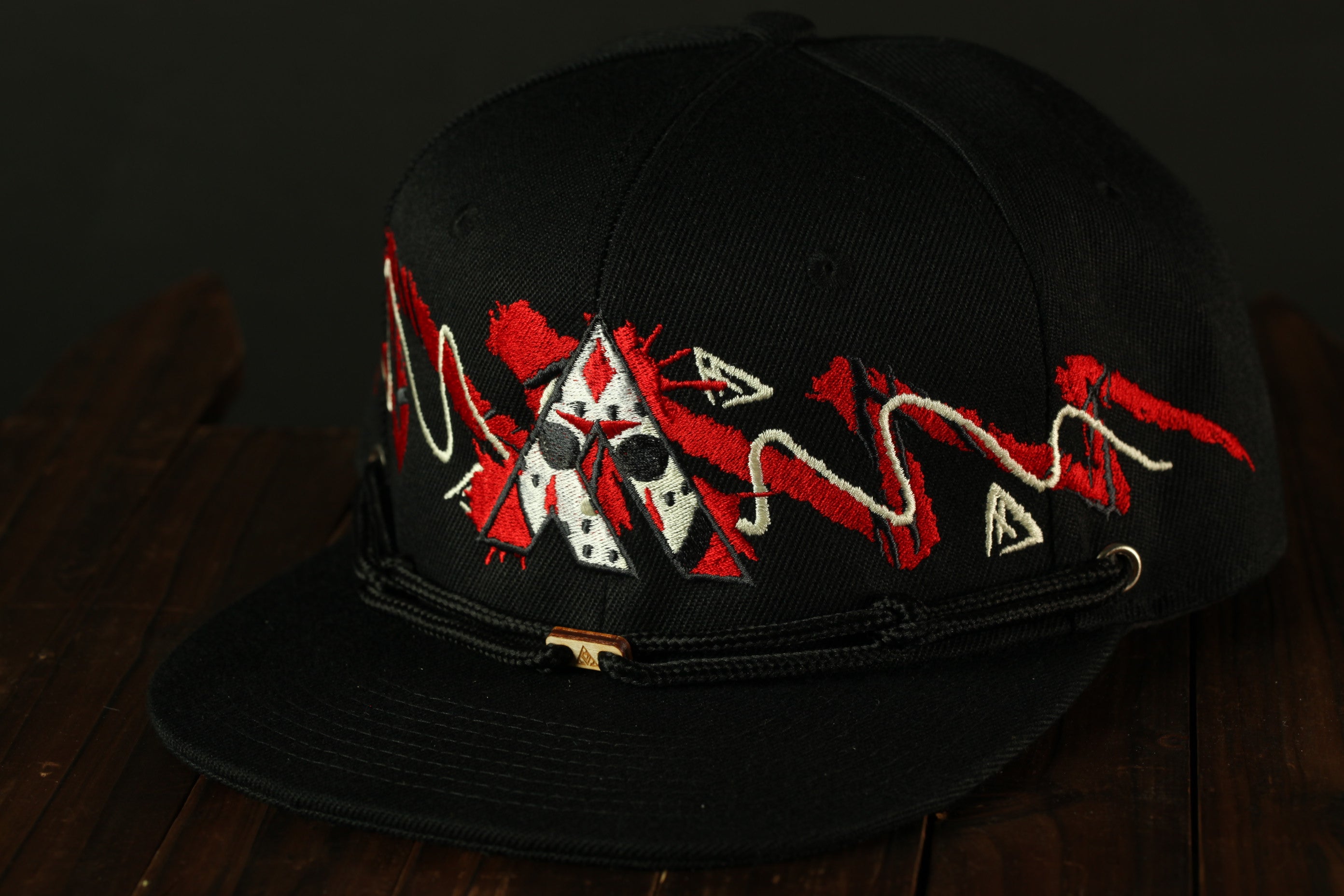 A black baseball cap with a red and white design on the front, sitting on a wooden surface.