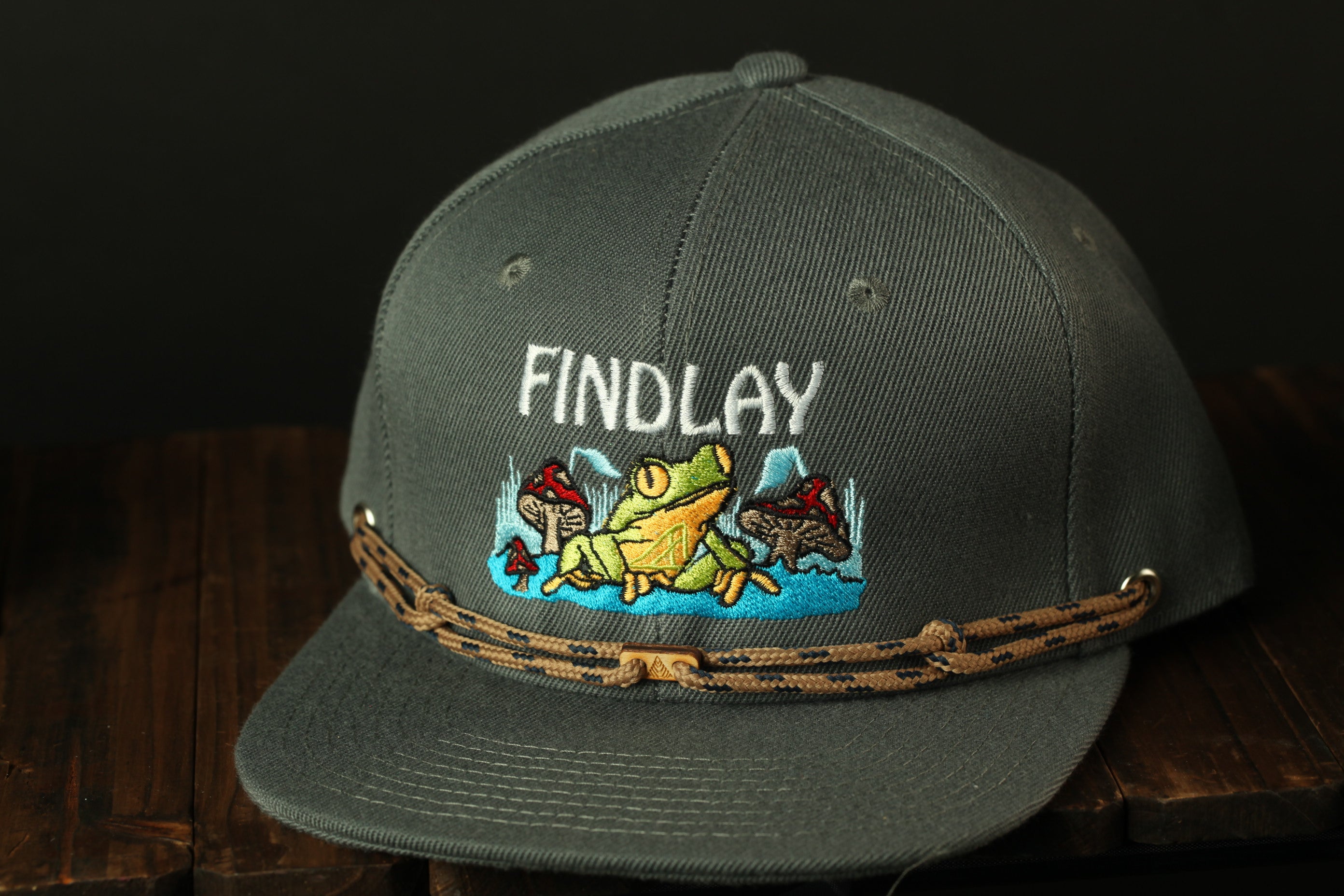 A gray baseball cap with a frog and mushroom embroidered on it, and the word "FINDLAY" printed on the front.