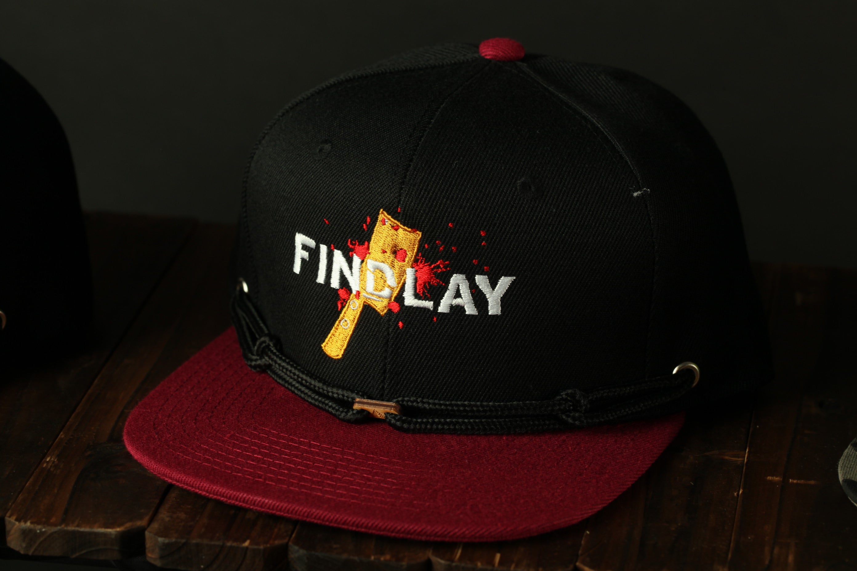 A black baseball cap with a red brim, featuring a graphic of a cross and the word "FINDlay" printed on it.