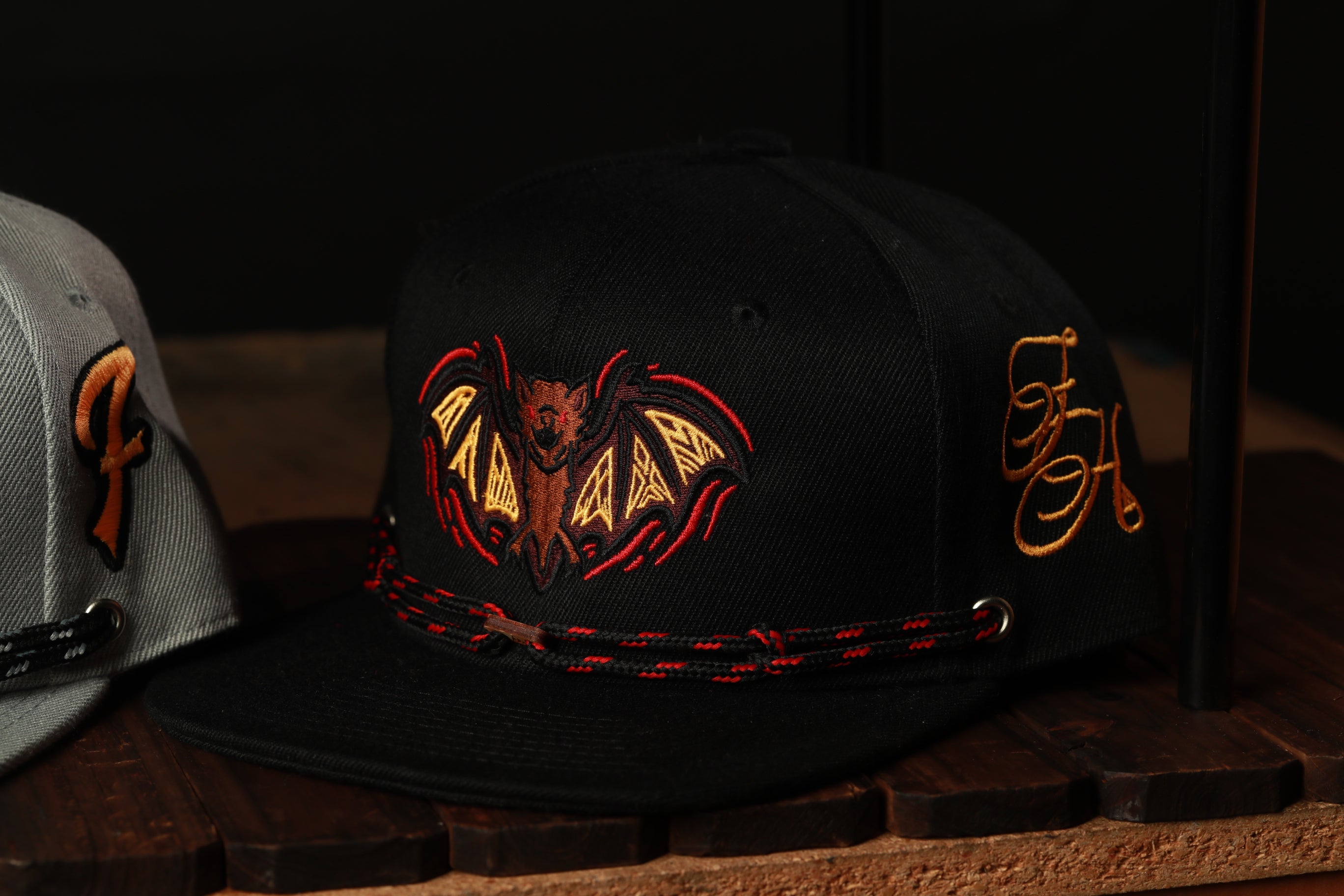 a black baseball cap with a bat design on it, placed on a wooden surface.