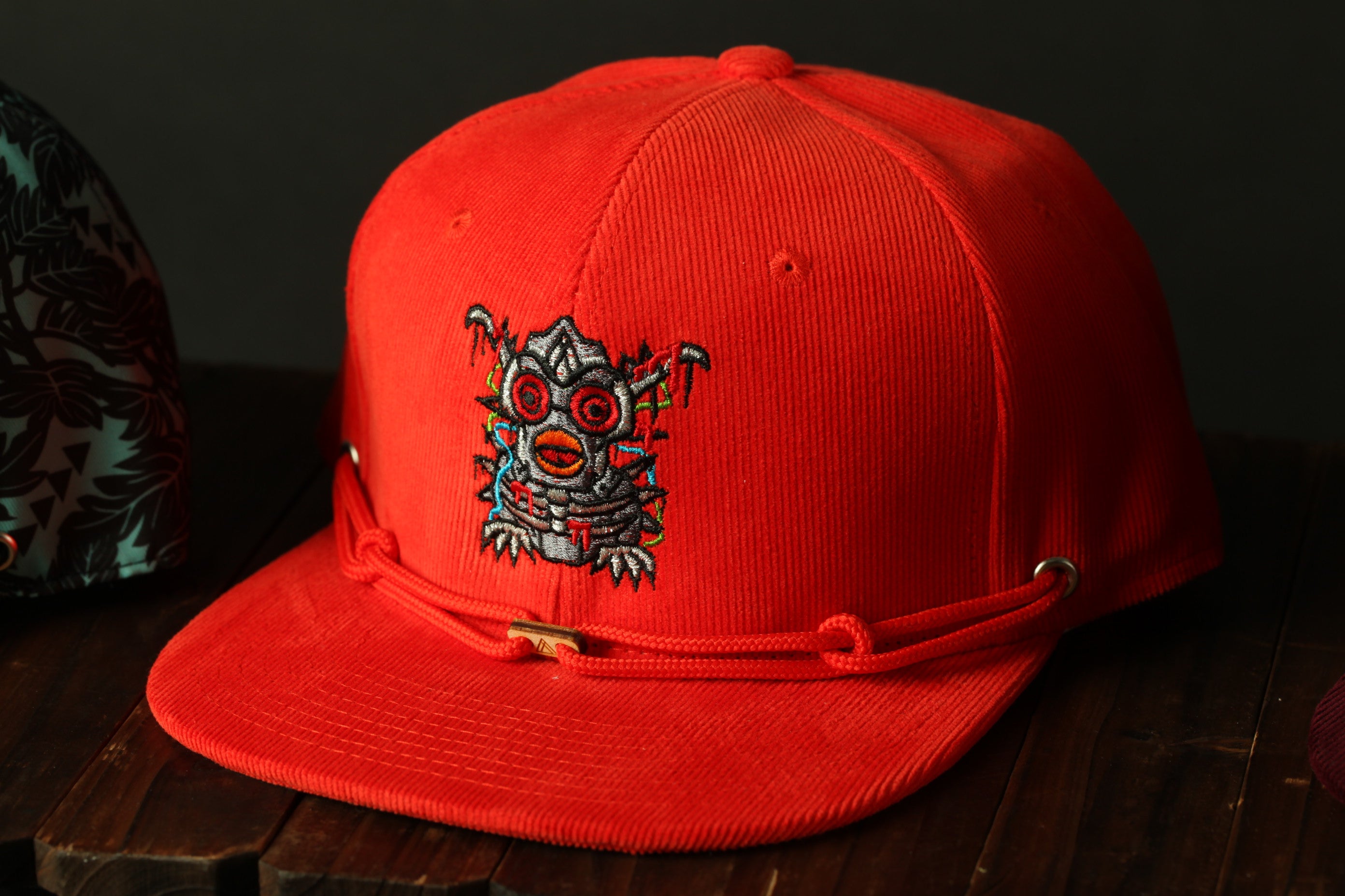 A red baseball cap with an embroidered design on the front, sitting on a wooden surface.