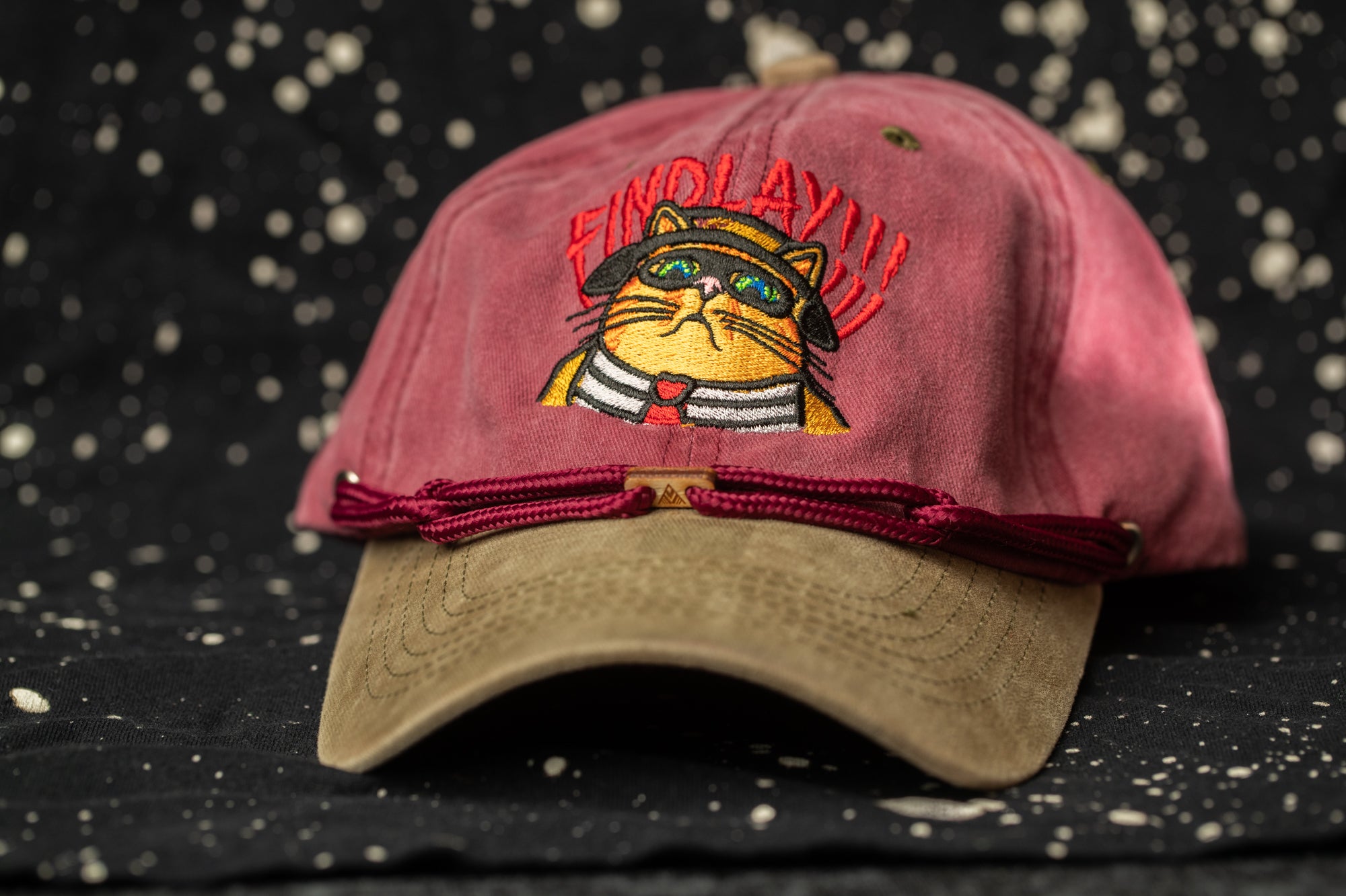 A red baseball cap with a cartoon cat design and the text "FIND LAY" printed on it.