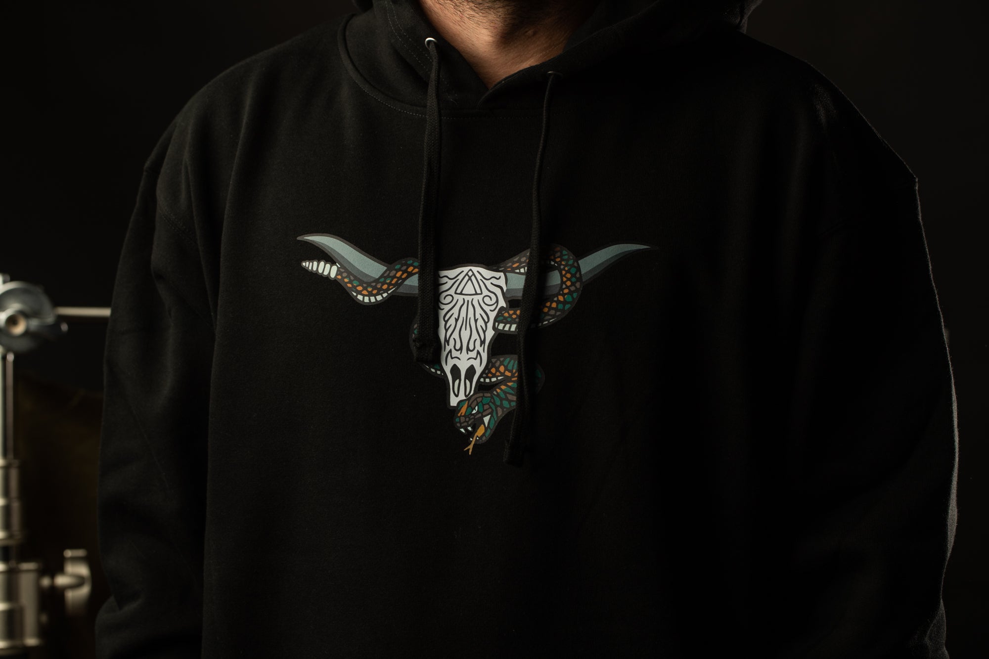A person wearing a black hoodie with a graphic design of a skull and a snake on it.