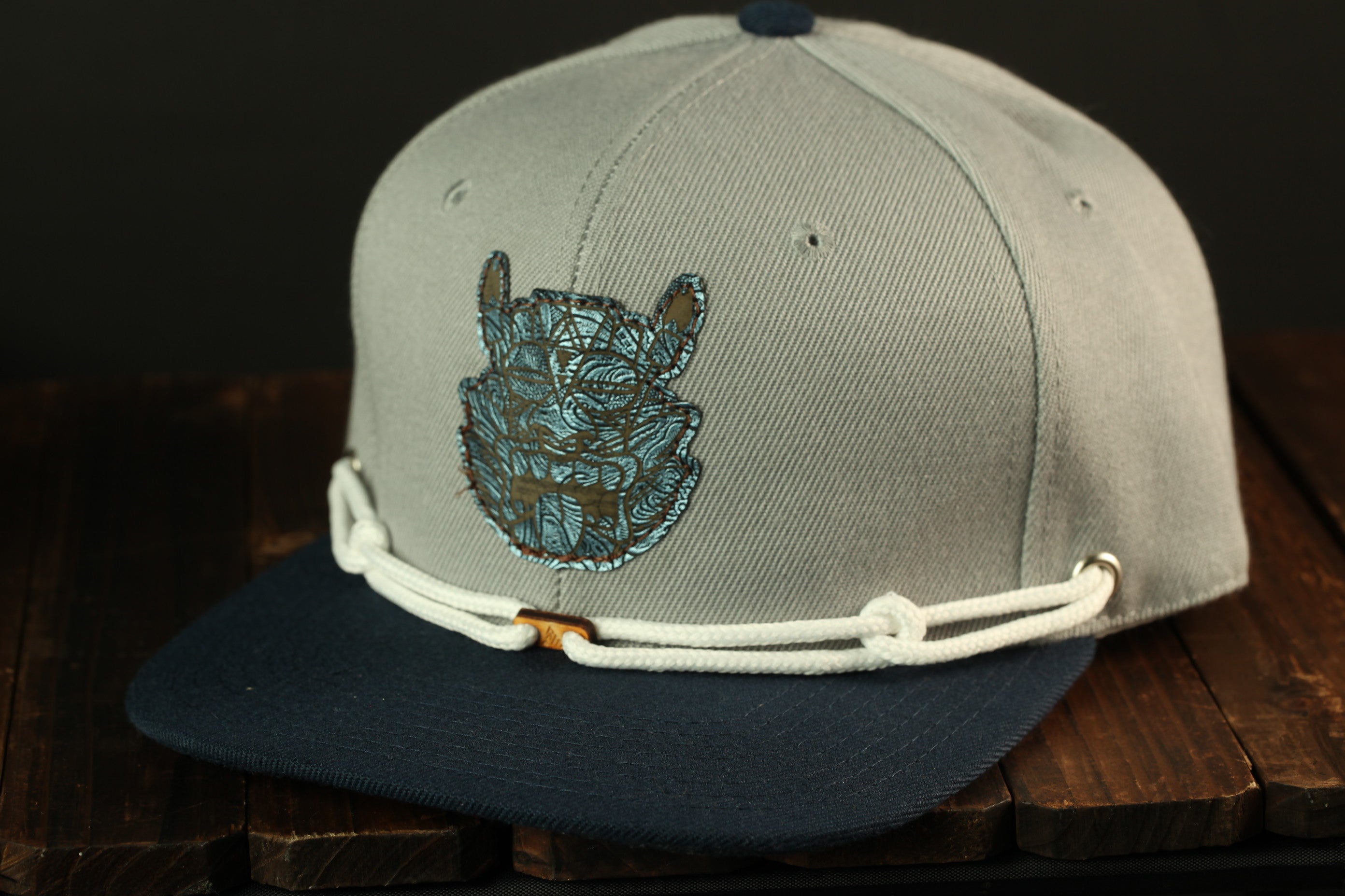 A gray baseball cap with a blue and white design on the front, sitting on a wooden surface.