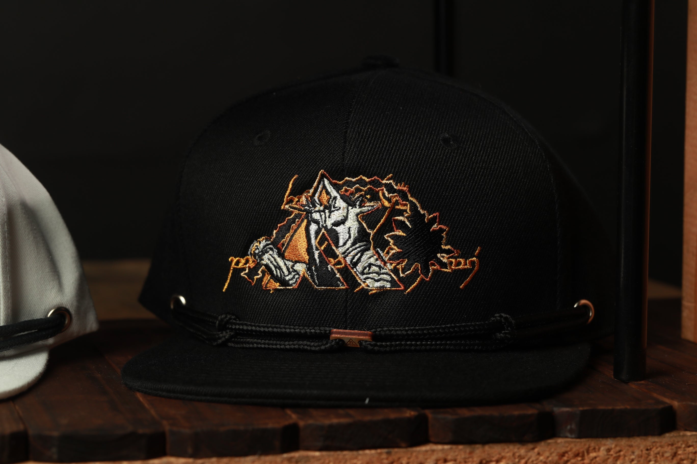 A black baseball cap with an embroidered design on the front, featuring a stylized figure or character.