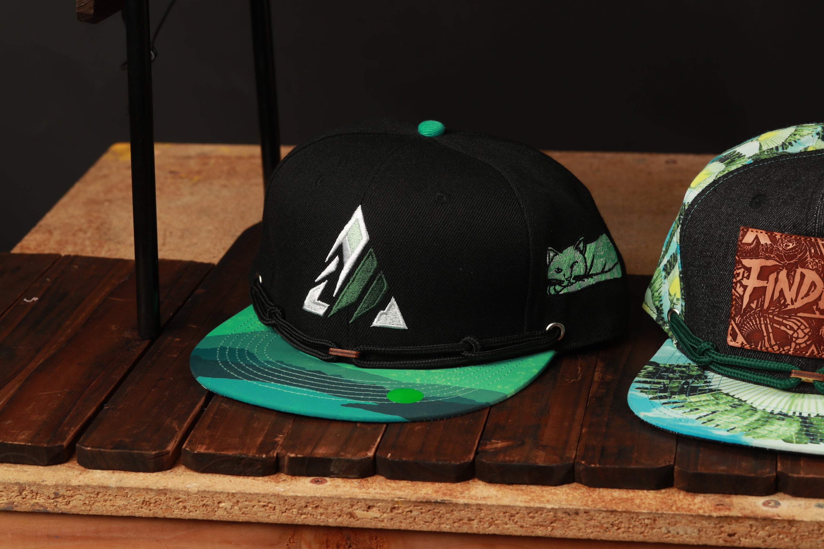 two baseball caps on a wooden surface, one black and one colorful with a patterned design.