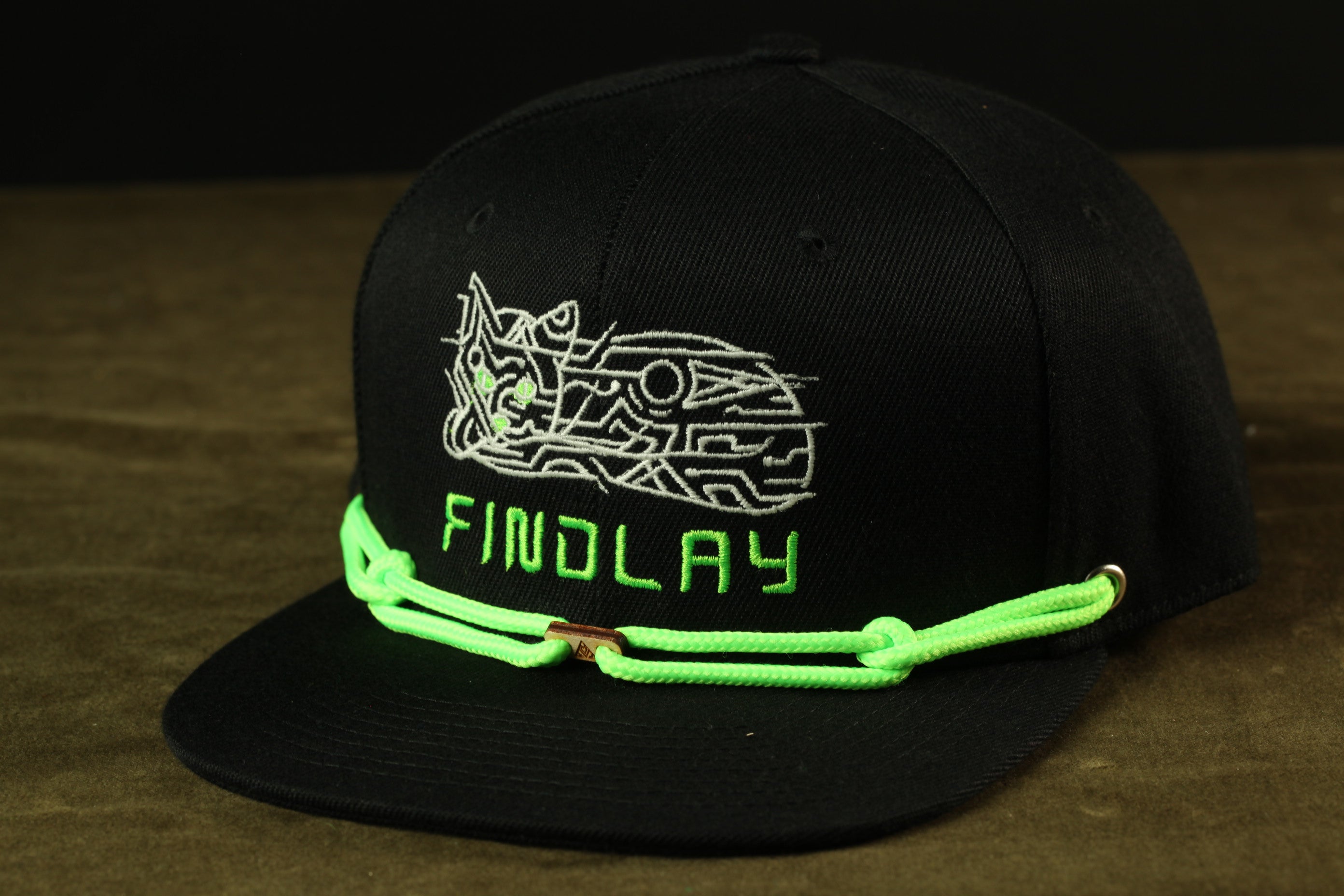 A black baseball cap with a neon green chain and the word "FINDLAY" printed on it.
