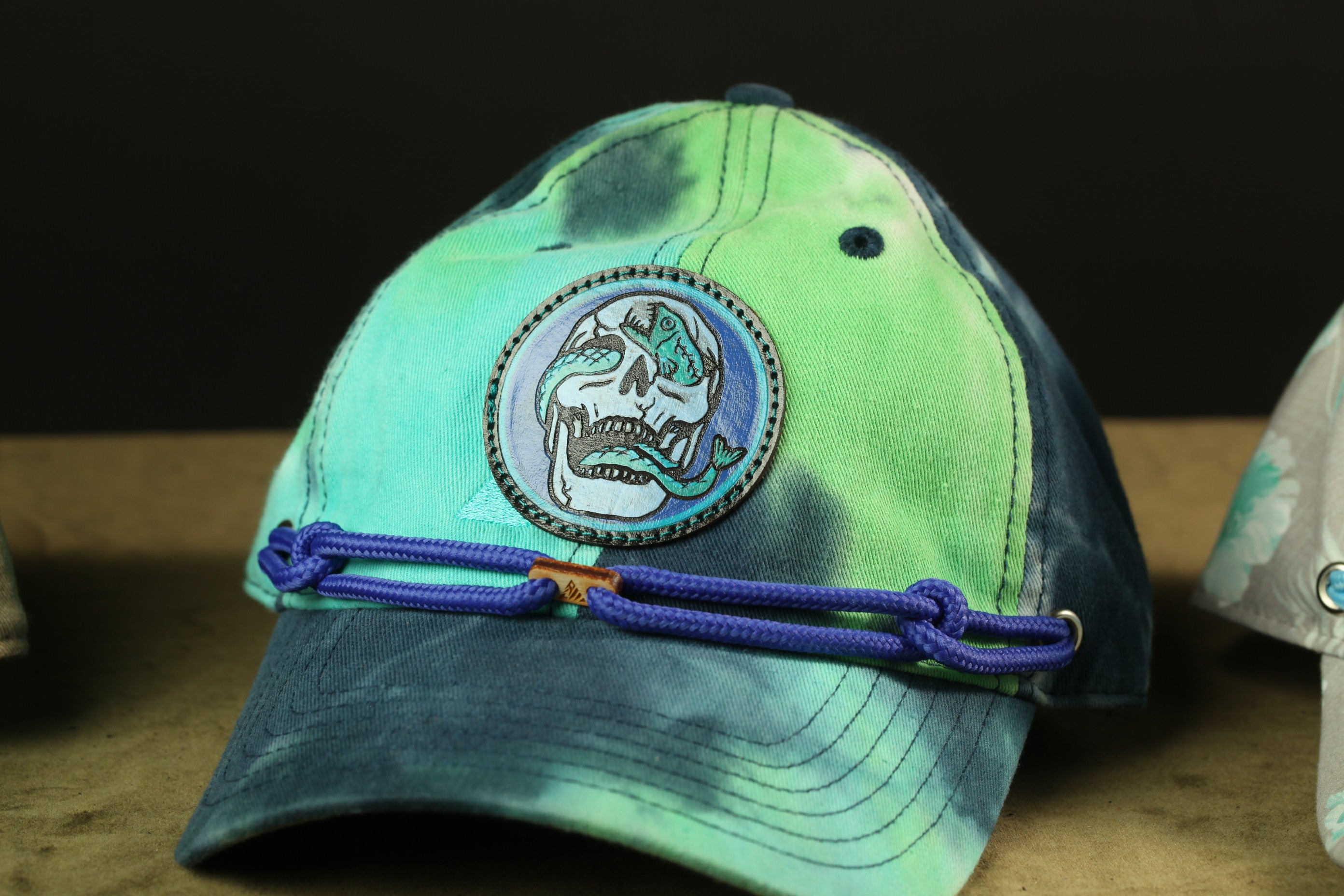 A tie-dye baseball cap with a skull patch and a blue string around the brim.
