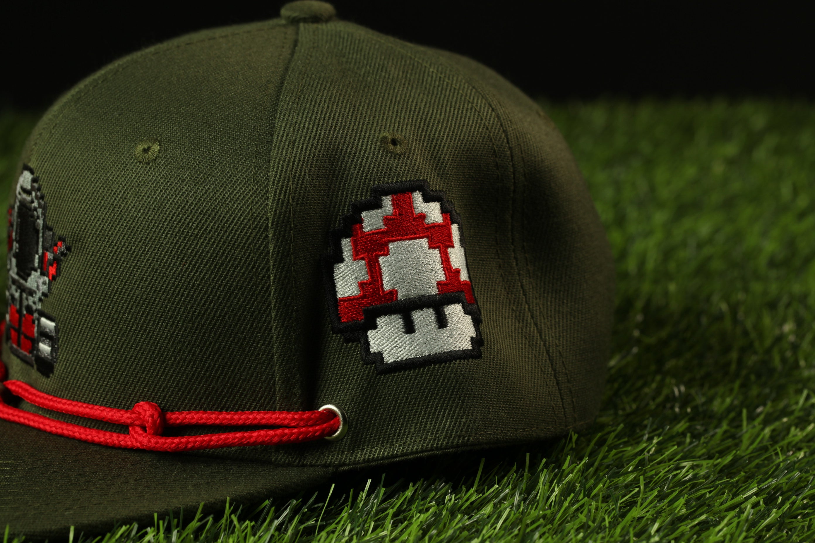 A green baseball cap with a mushroom-shaped patch on the side, lying on a grassy surface.