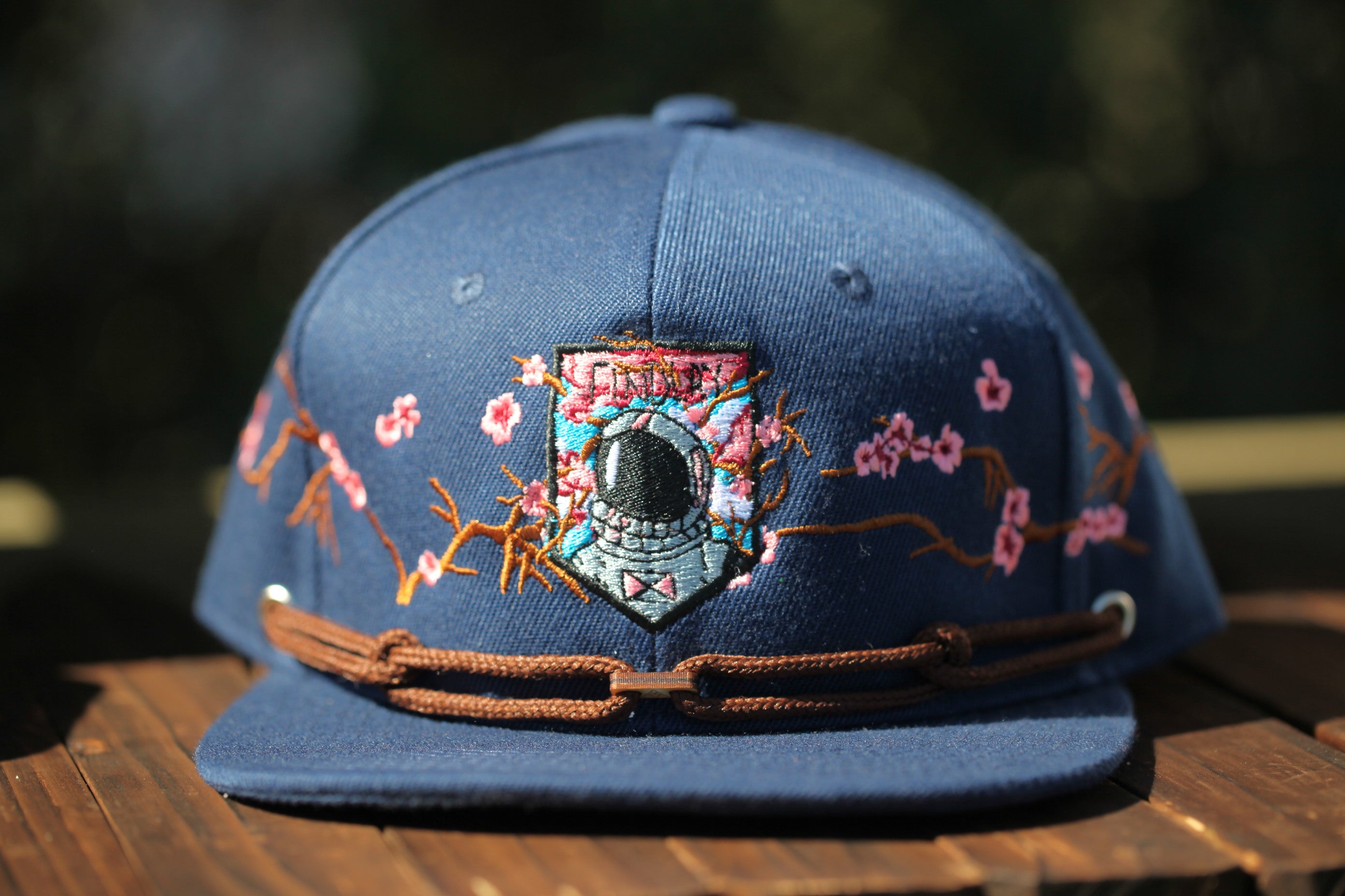 A blue baseball cap with a floral design and a small emblem on the front, sitting on a wooden surface.