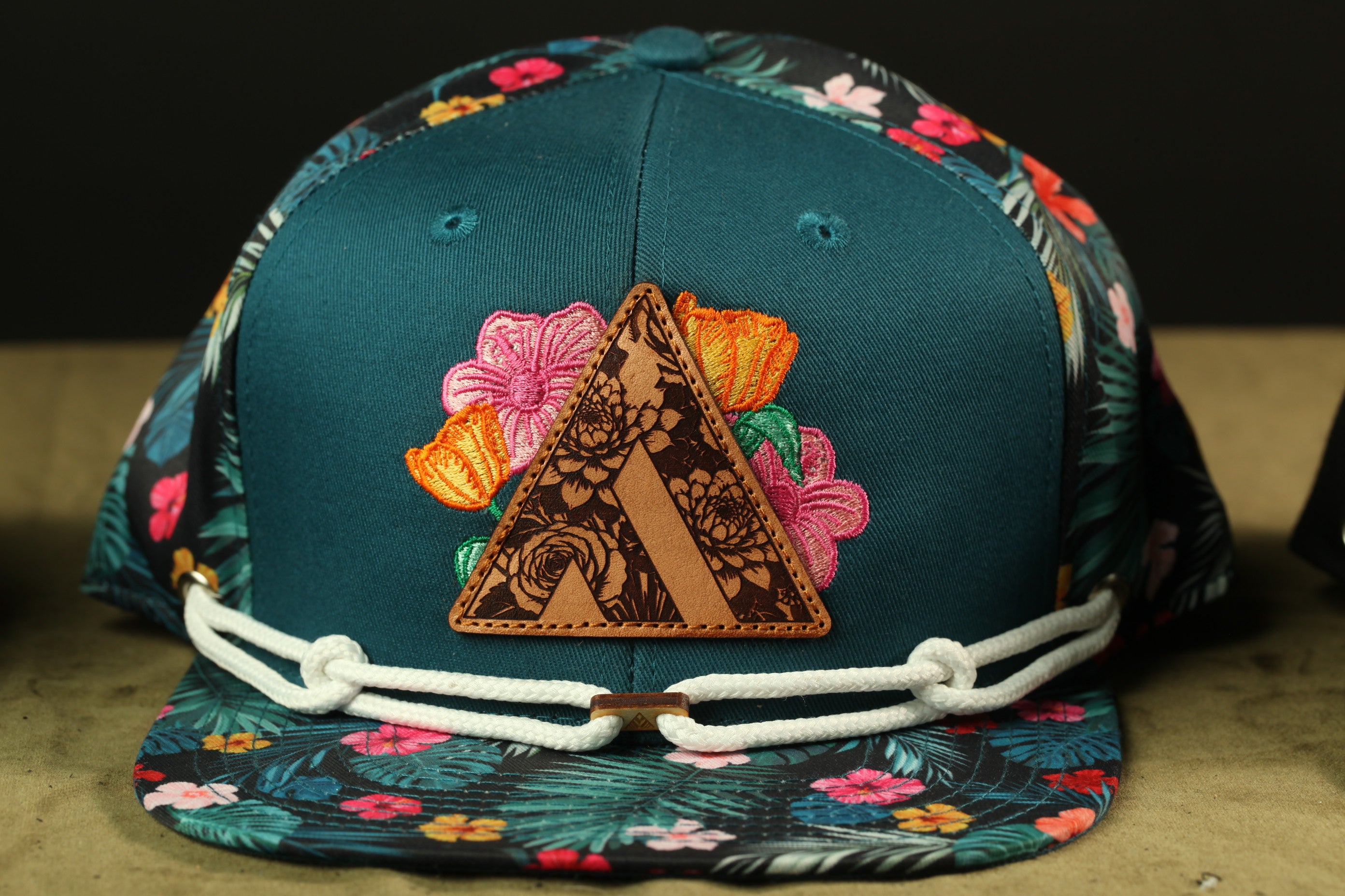 A colorful floral-patterned baseball cap with a leather patch featuring a floral design.