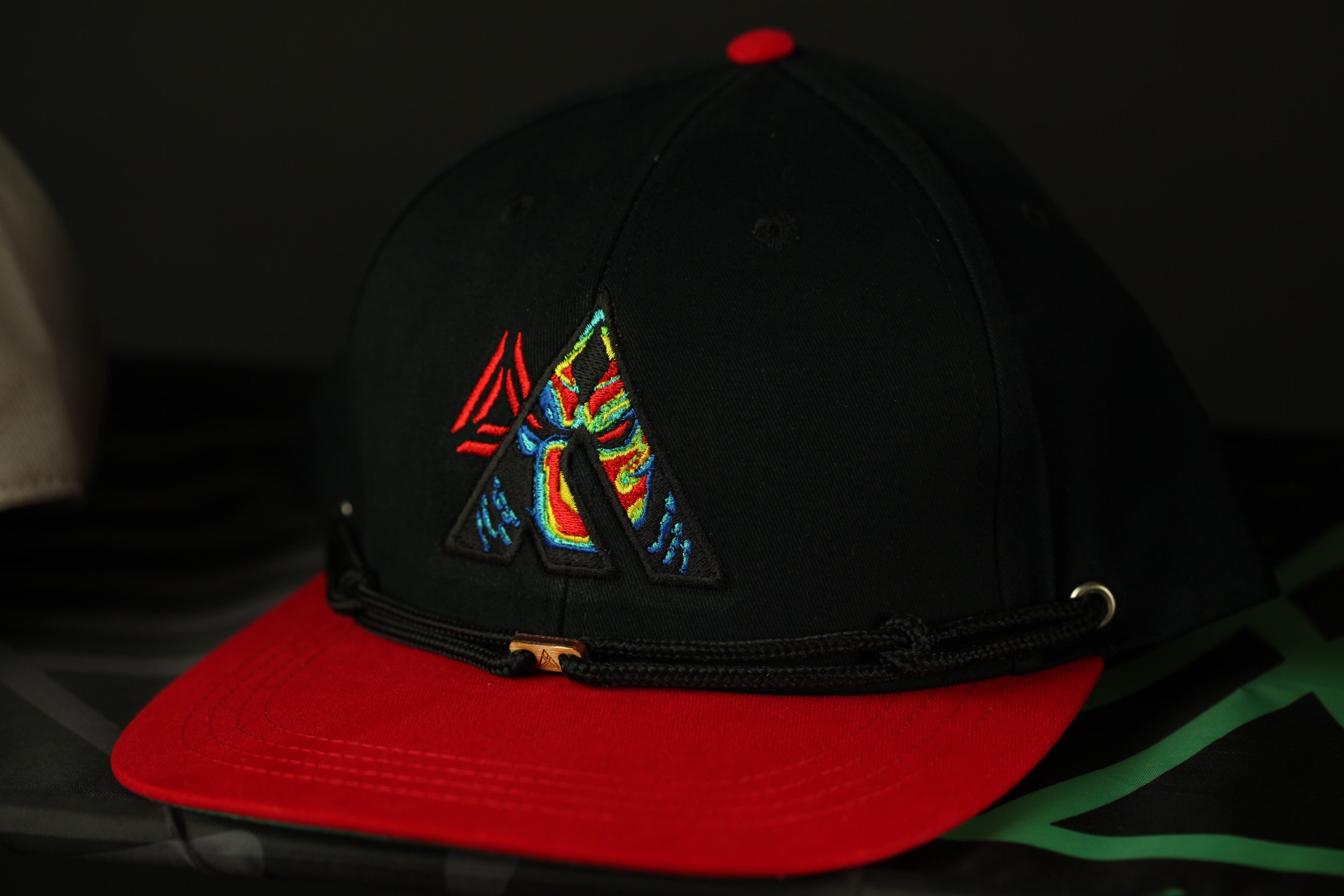 A black baseball cap with a red brim and a colorful, abstract design on the front.