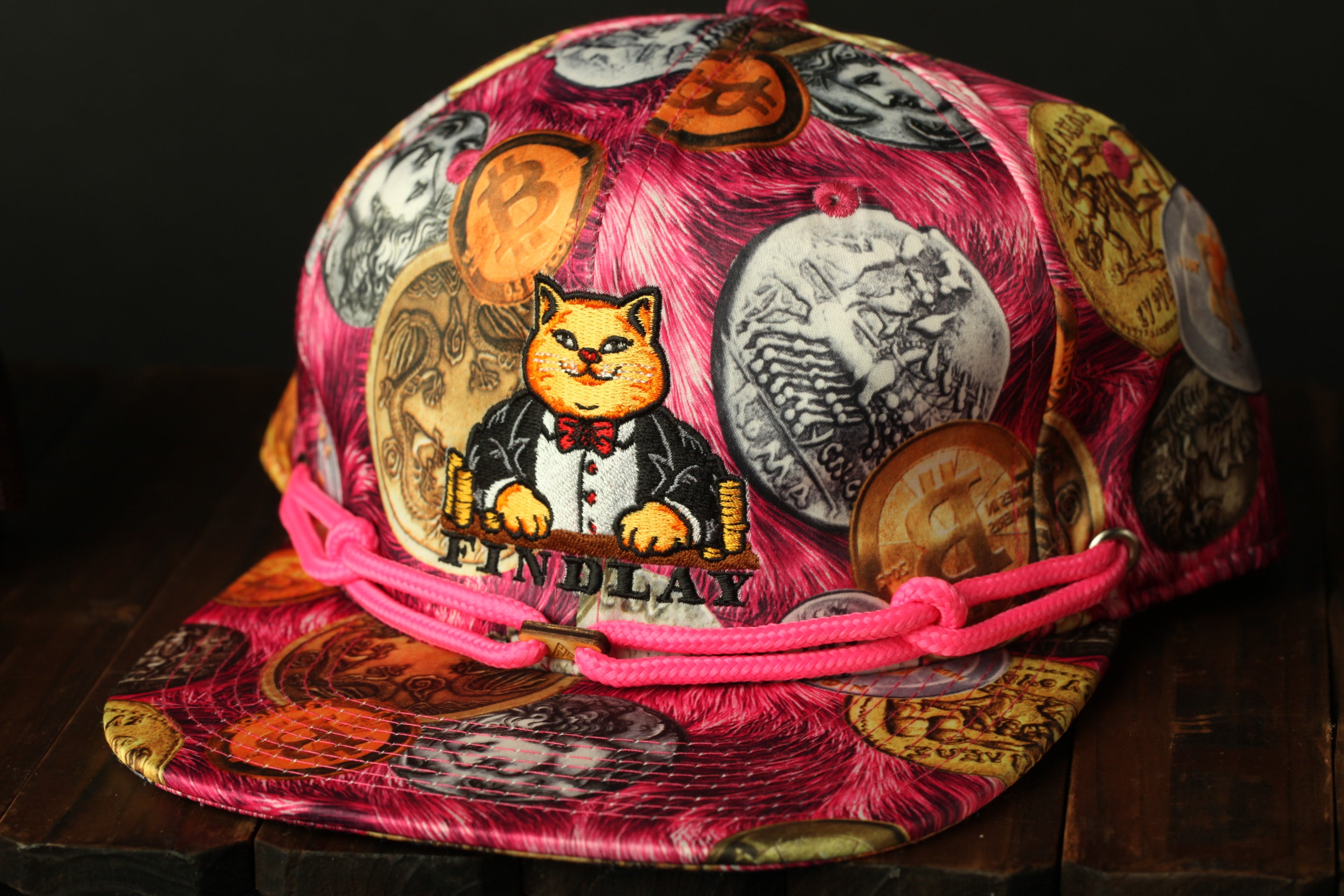 A colorful, patterned baseball cap with a cat design and various coins printed on it.