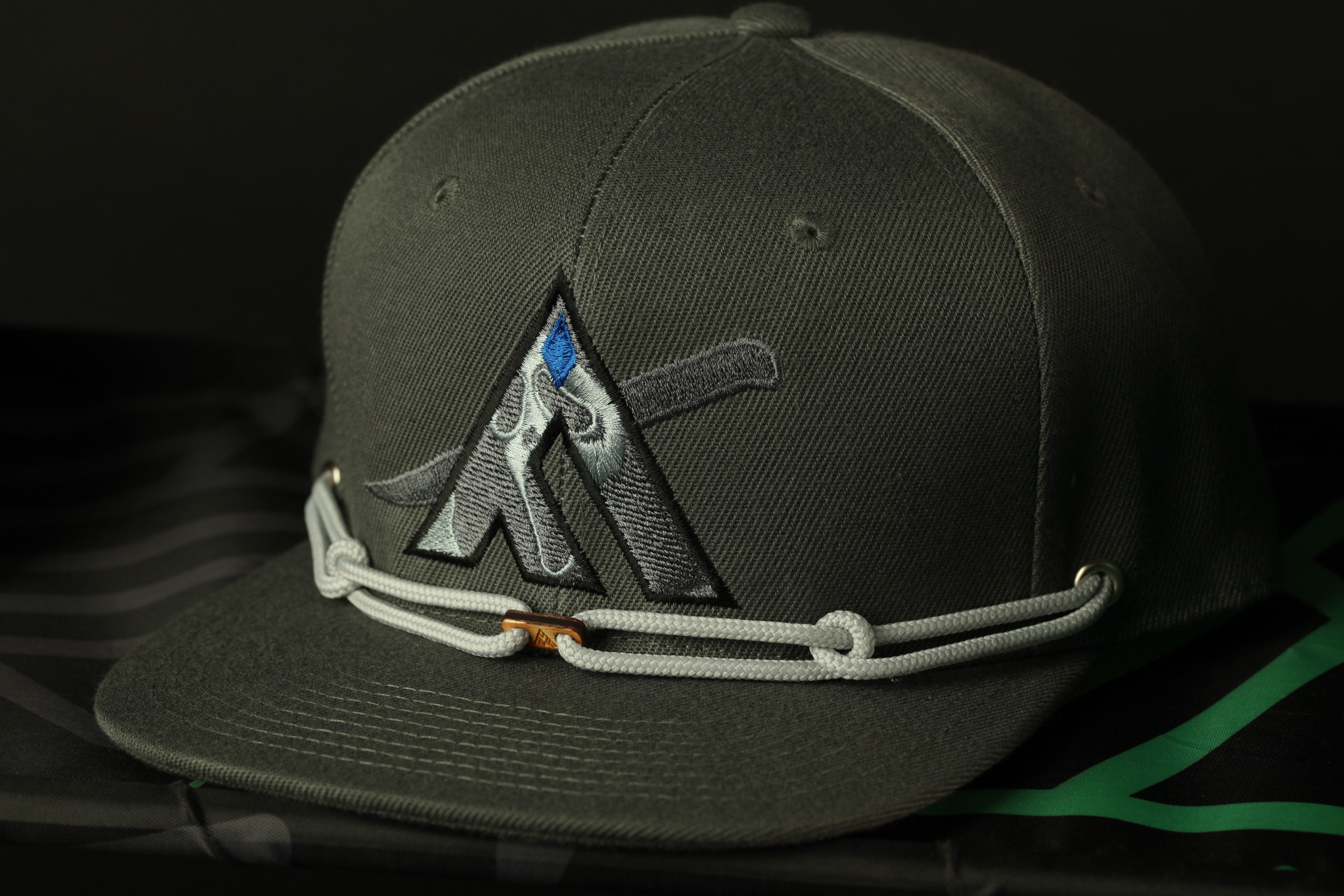 A close-up image of a dark green baseball cap with a unique logo on the front.