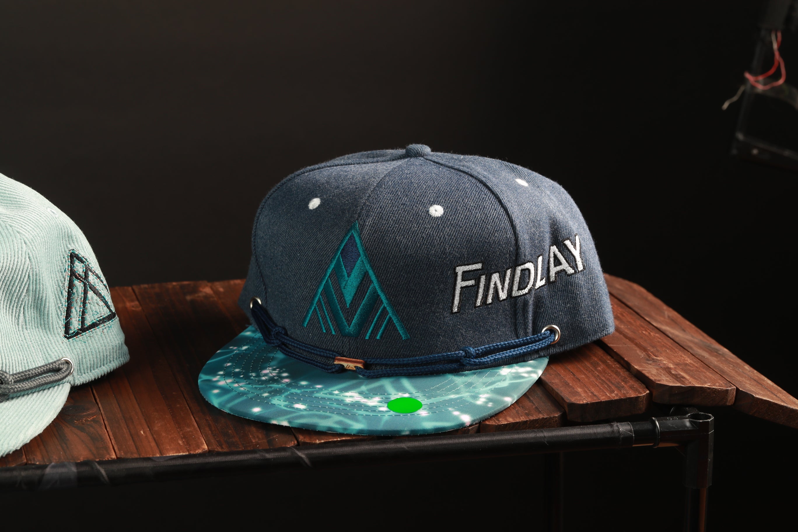 A blue baseball cap with the word "Findlay" printed on it, placed on a wooden surface.