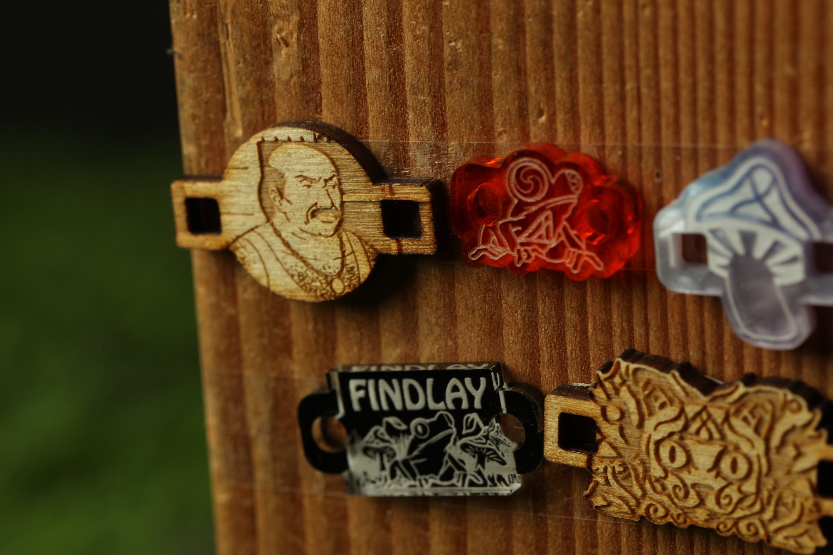a wooden board with various wooden objects attached to it, including a wooden bead with a man's face, a wooden bead with a red frog, and a wooden bead with a mushroom.