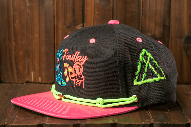 A black baseball cap with colorful embroidered designs and a pink brim, placed on a wooden surface.