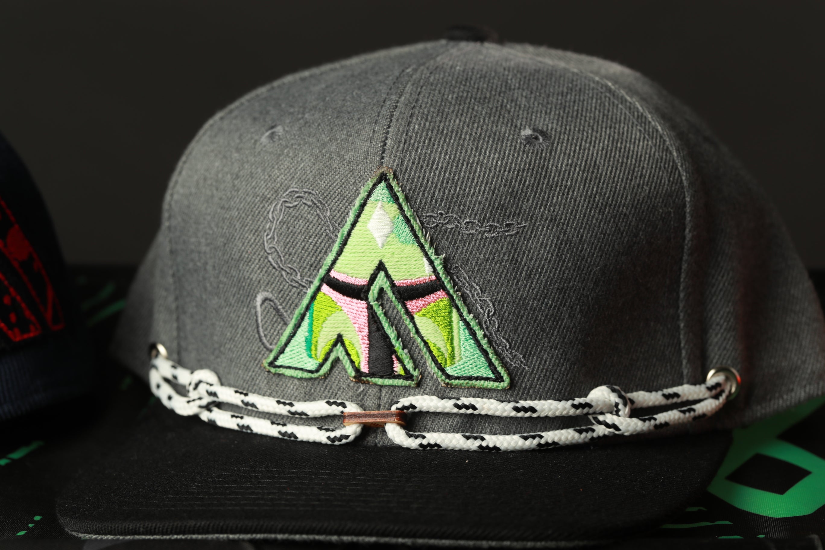 A gray baseball cap with a green and pink embroidered logo on the front.