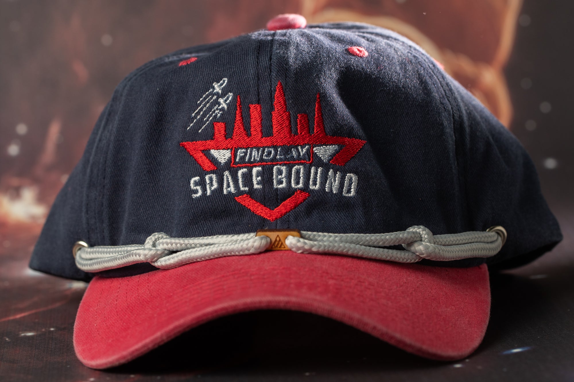 A navy blue baseball cap with a red brim and a logo that says "FIND A SPACE BOUND" on it.