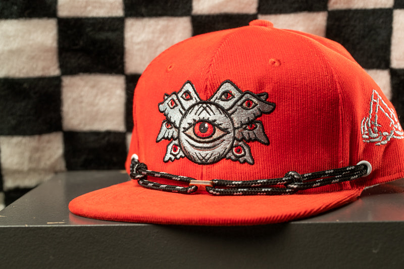 A red baseball cap with a black and white checkered pattern and an eye design on the front.