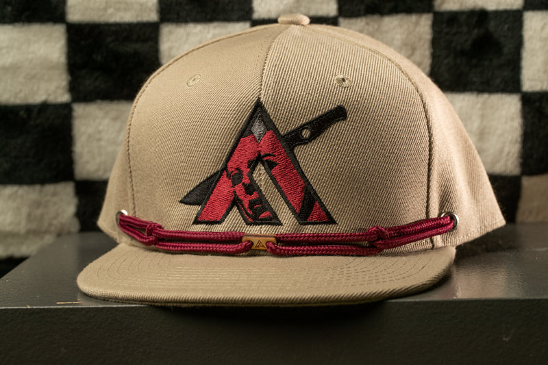 A beige baseball cap with a red and black logo on the front, displayed on a gray surface against a black and white checkered background.
