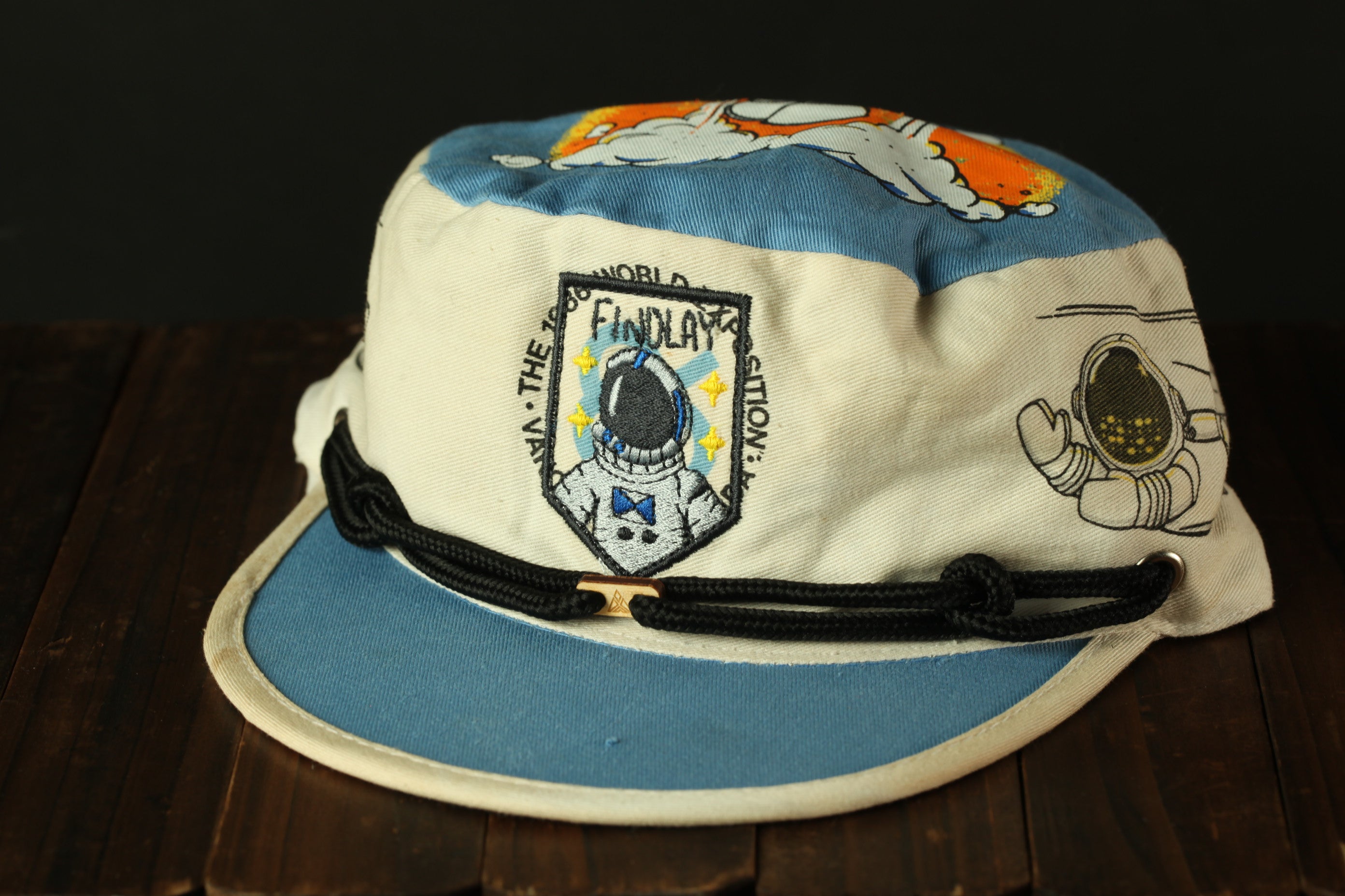 A colorful baseball cap with an astronaut design and the text "FIND THE WORLD" printed on it.