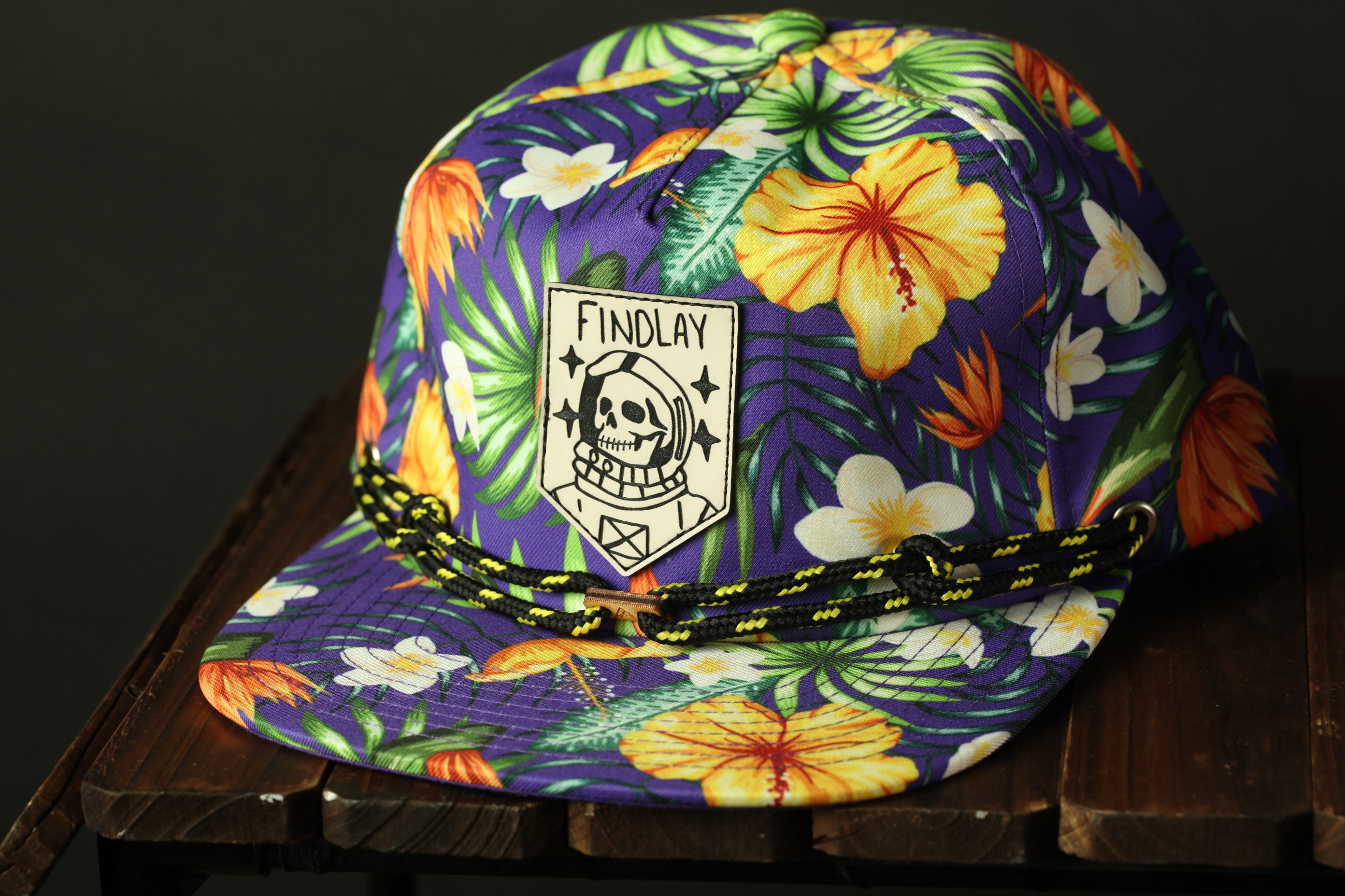 A colorful, patterned baseball cap with a skull and floral design, sitting on a wooden surface.