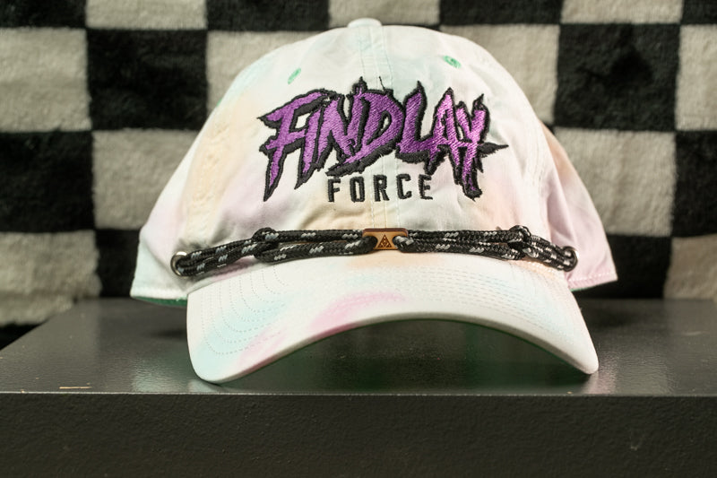 A white baseball cap with purple and black text on it, sitting on a black surface against a checkered background.