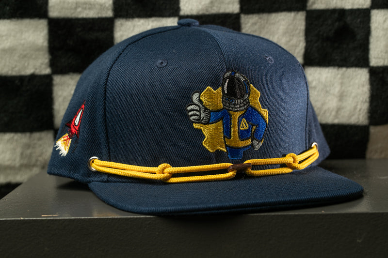 A navy blue baseball cap with a yellow chain strap and a graphic of a character wearing a blue suit and helmet.