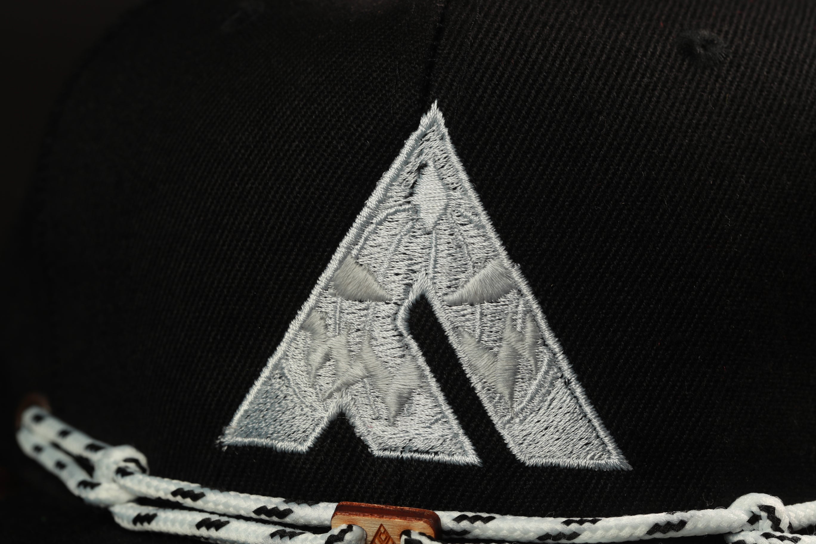 A close-up view of a black baseball cap with a white embroidered logo on the front.