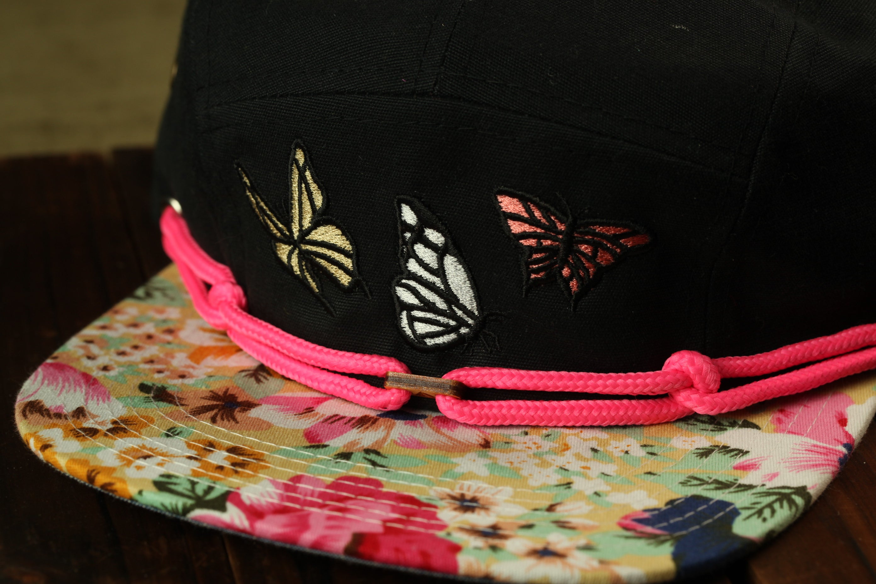 A close-up image of a black baseball cap with colorful butterfly embroidery on the front.
