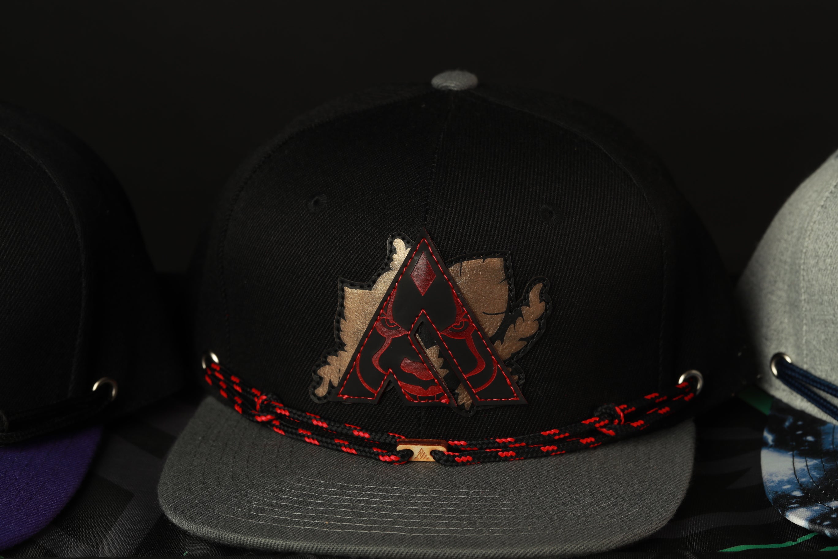 A black baseball cap with a red and gold logo on the front, sitting on a gray brim.