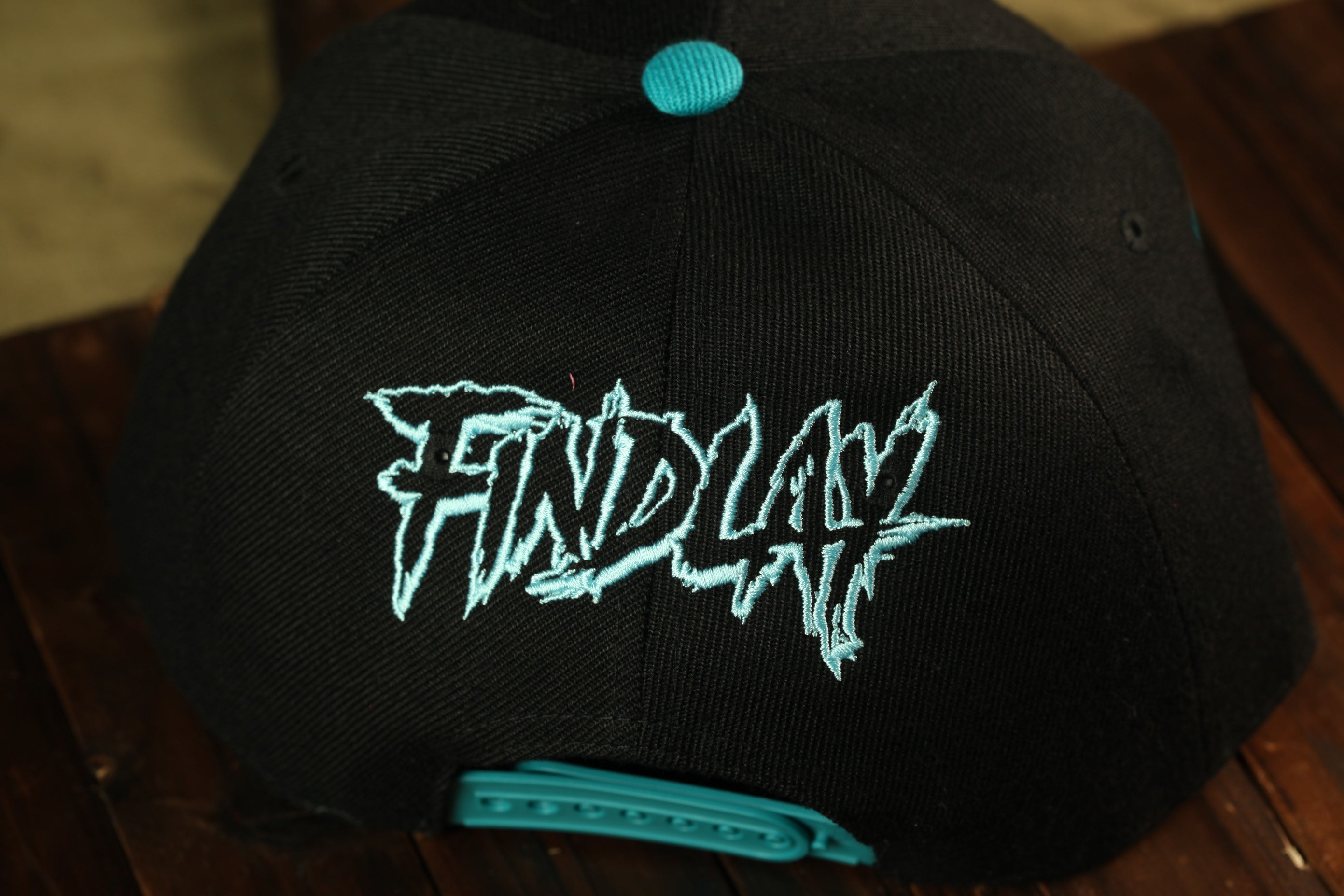A black baseball cap with teal stitching and the word "FIND" embroidered on it.