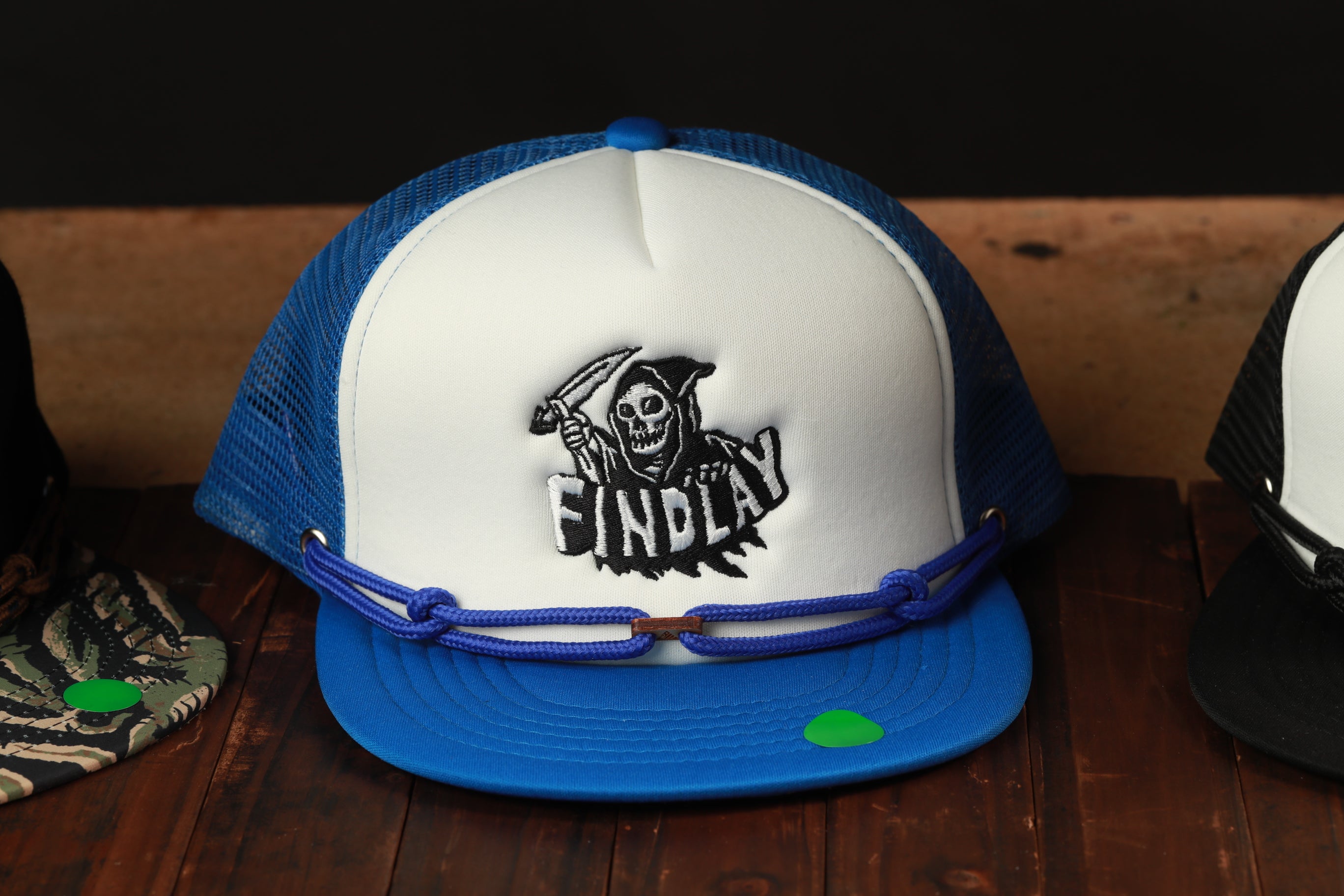 A blue and white baseball cap with a skull and crossbones design, featuring the word "FINDlay" on the front.