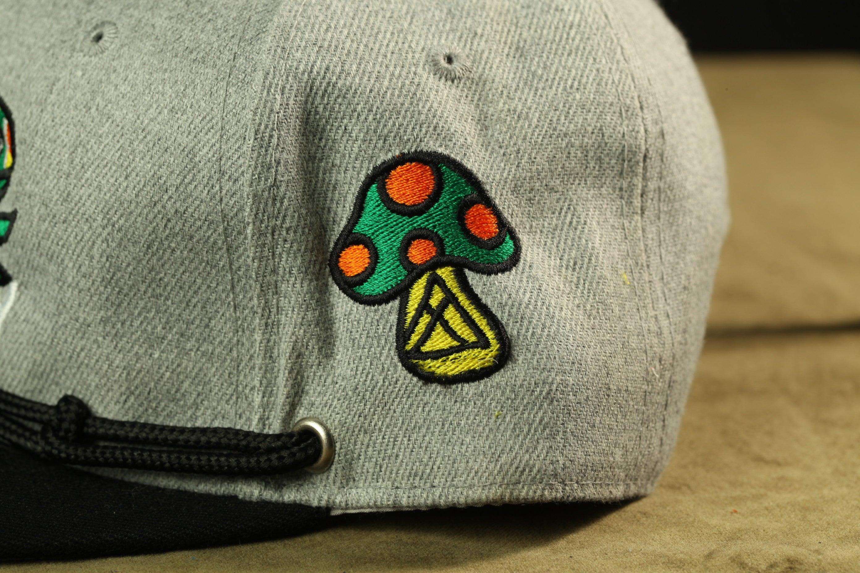 A close-up view of a gray baseball cap with a colorful mushroom-shaped embroidered patch on the front.