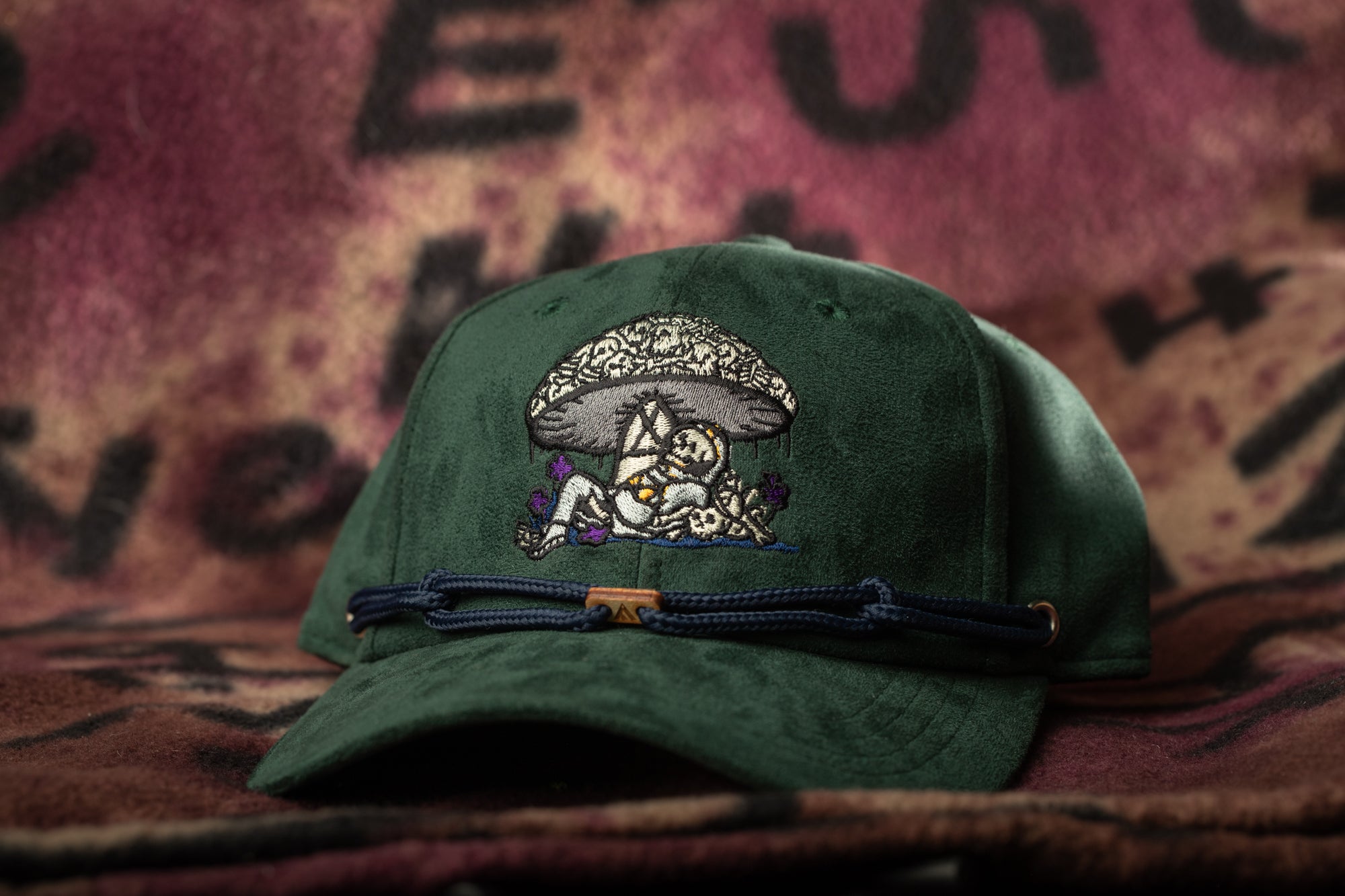 A green baseball cap with an embroidered design on the front, featuring a mushroom and a person, is displayed against a colorful background.