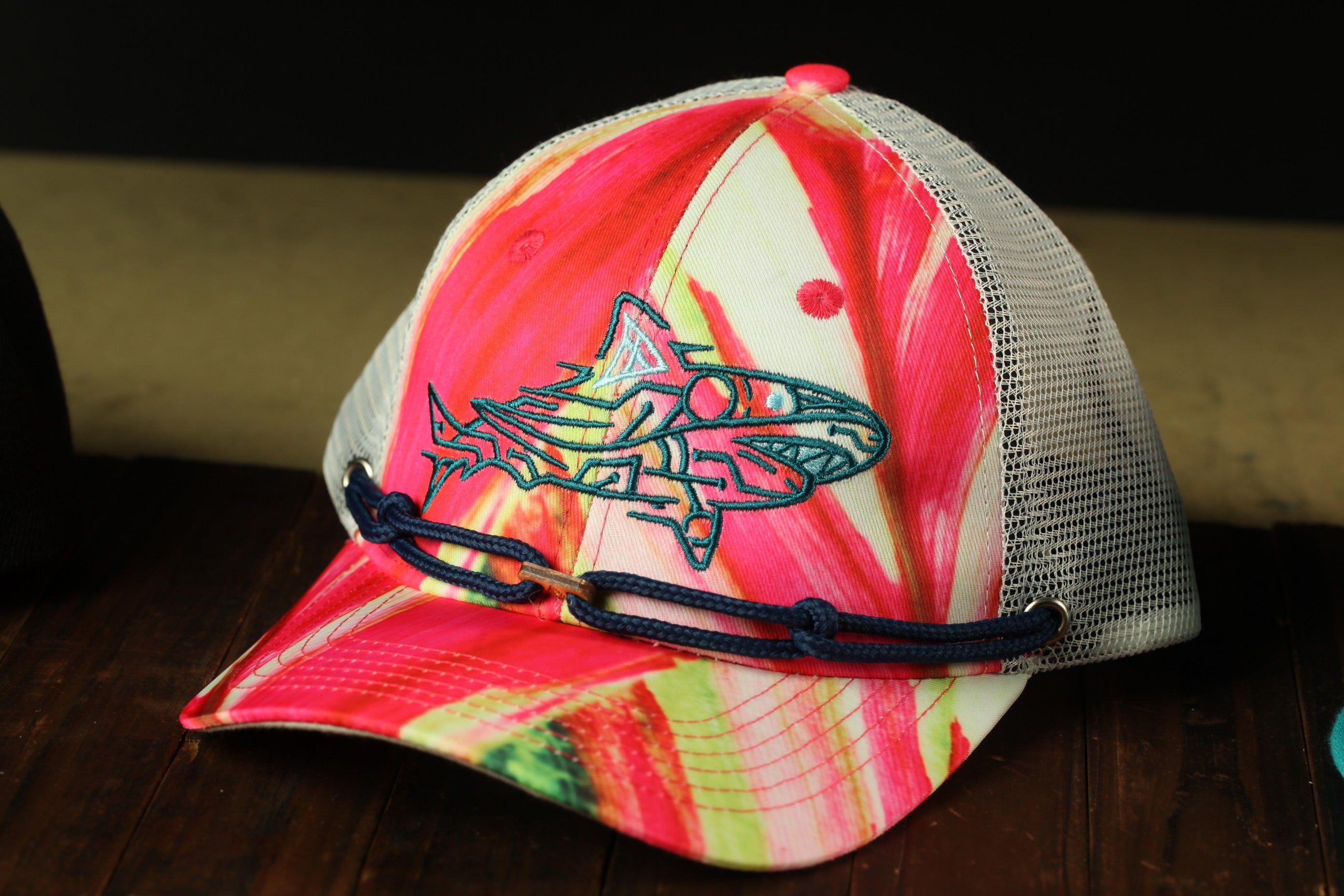 A colorful, patterned baseball cap with a shark design on the front, sitting on a wooden surface.