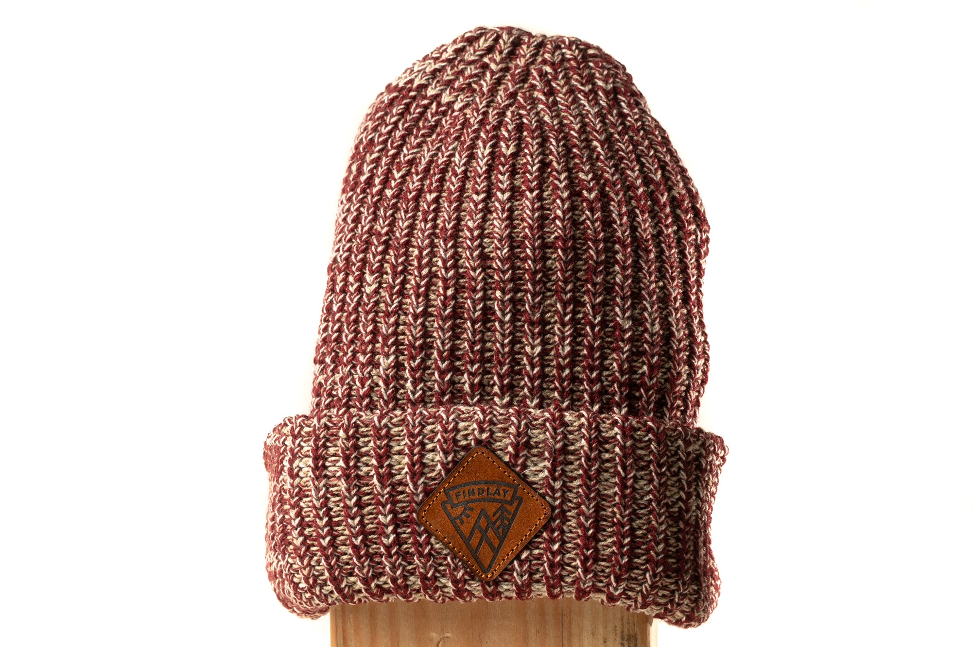 A red and white knitted beanie with a brown leather patch on the front.