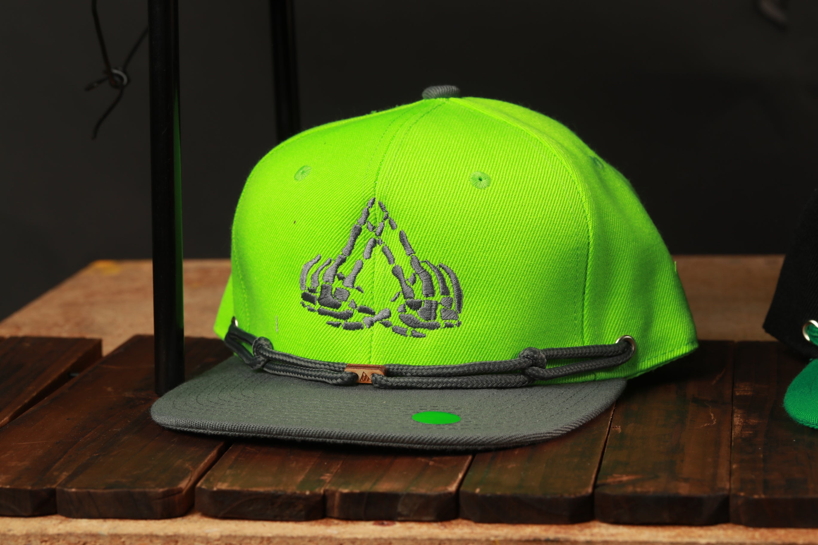 A neon green baseball cap with a skeleton hand embroidered on it, placed on a wooden surface.