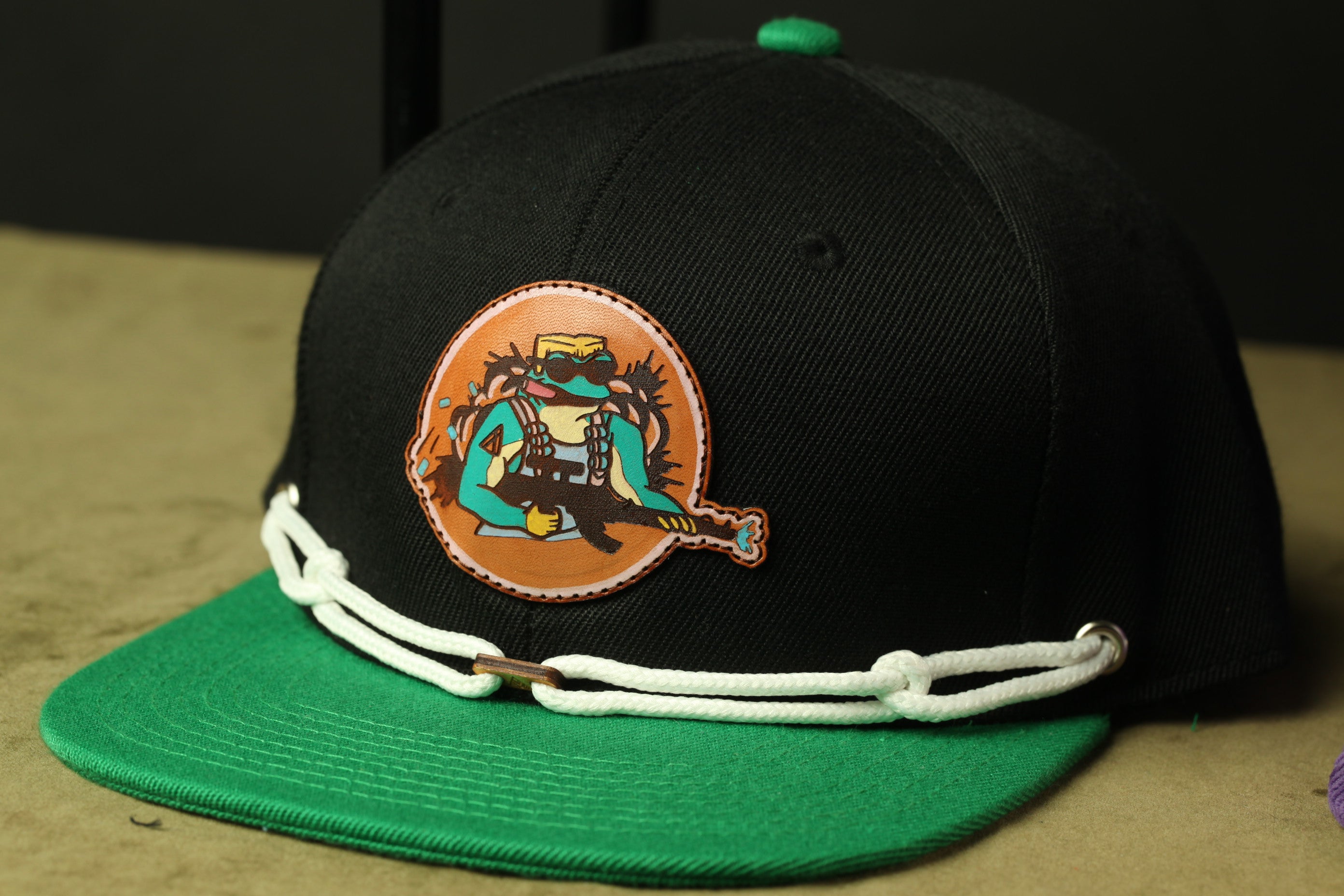 A black baseball cap with a colorful graphic patch on the front, featuring a cartoon character.