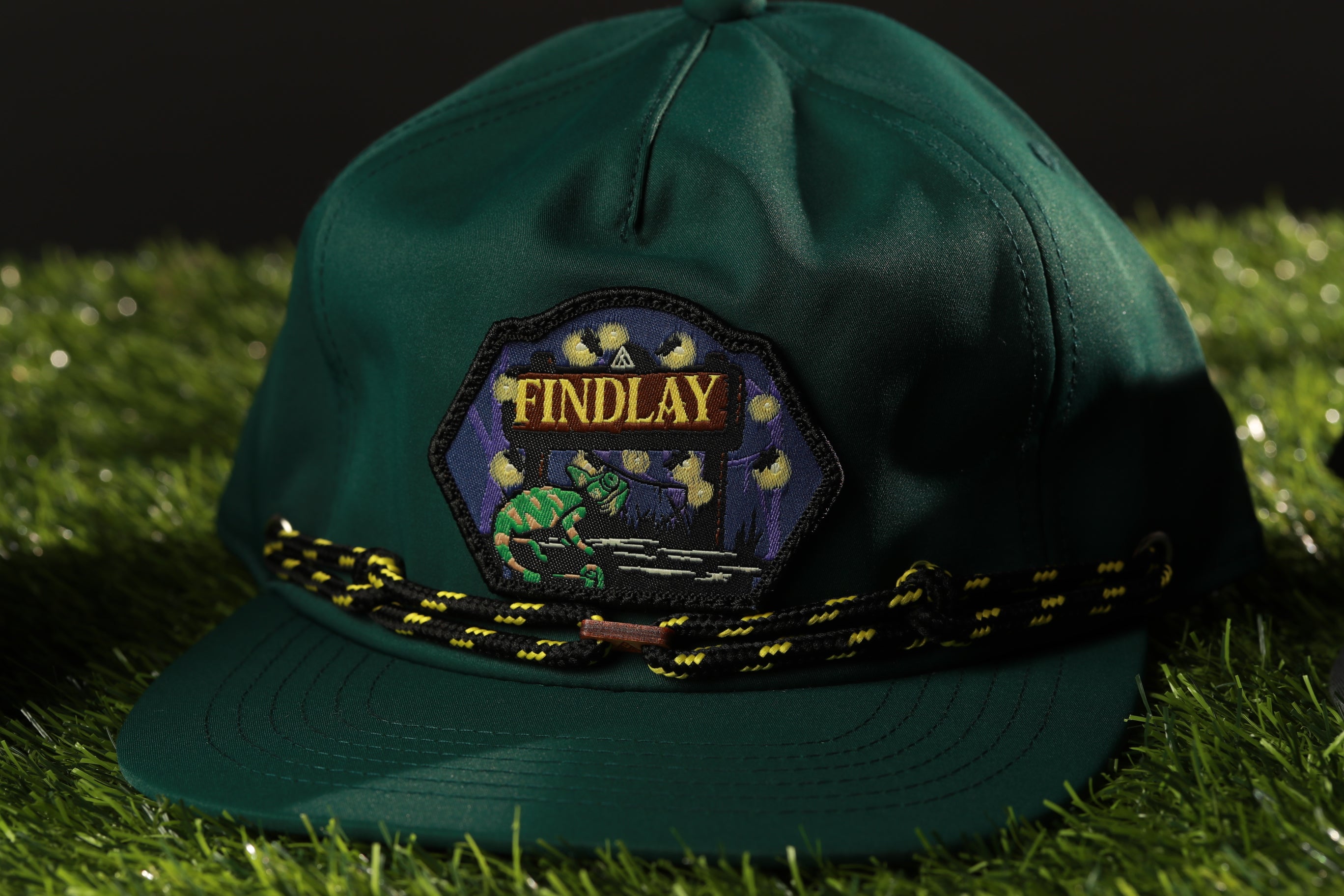 A green baseball cap with a patch on the front, featuring a chameleon and the word "FINDLAY" written on it.