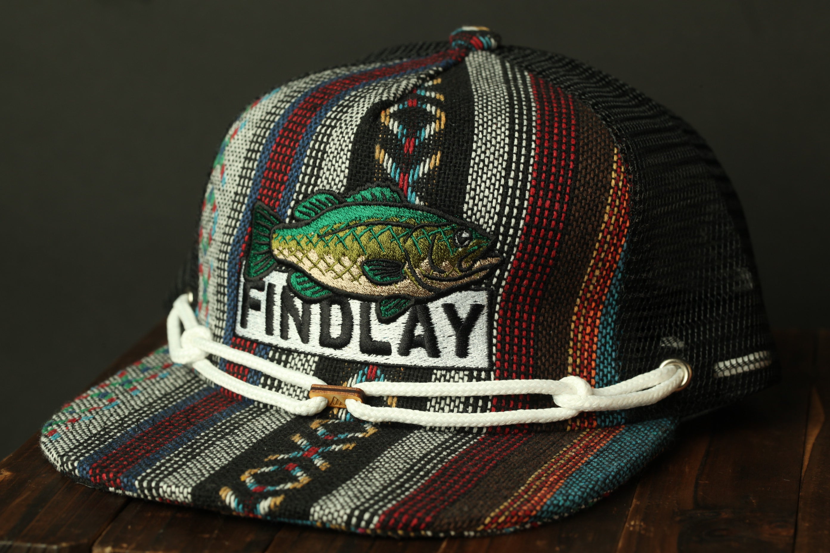 A colorful, patterned baseball cap with a fish embroidered on it, featuring the word "FINDLAY" on the front.