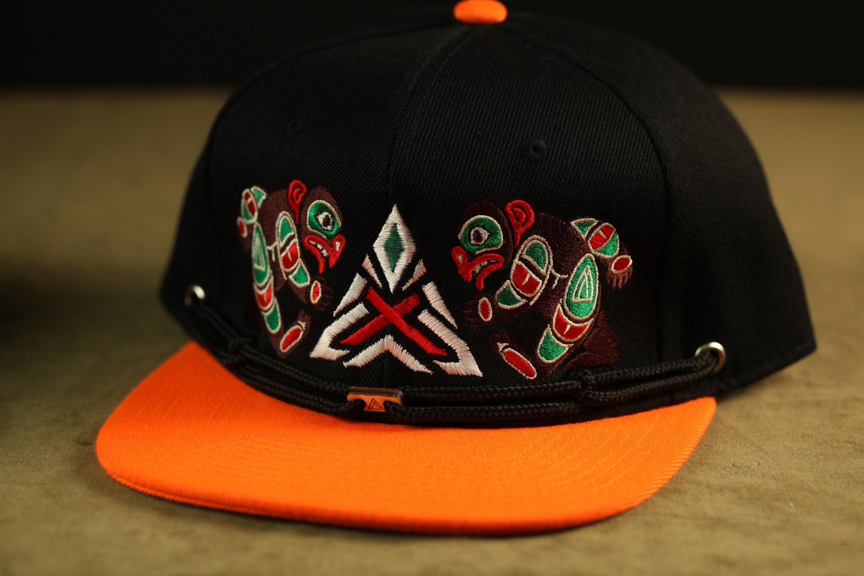 A black baseball cap with an orange brim, featuring colorful, abstract designs on the front.
