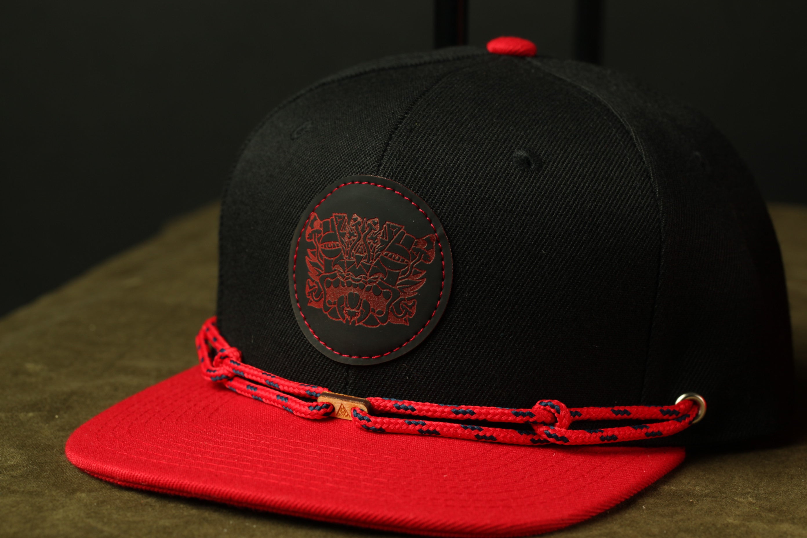 A black baseball cap with a red brim and a red and black chain strap.
