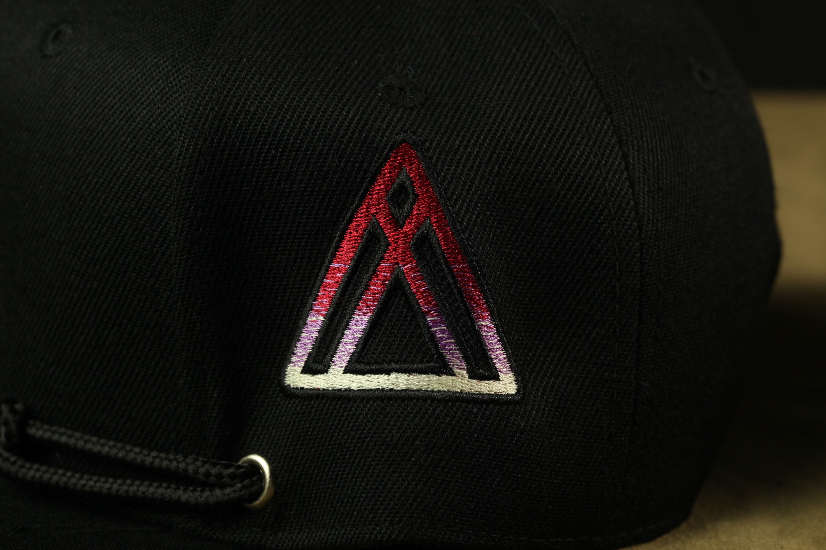 A close-up view of a black baseball cap with a red and white triangle embroidered on the front.