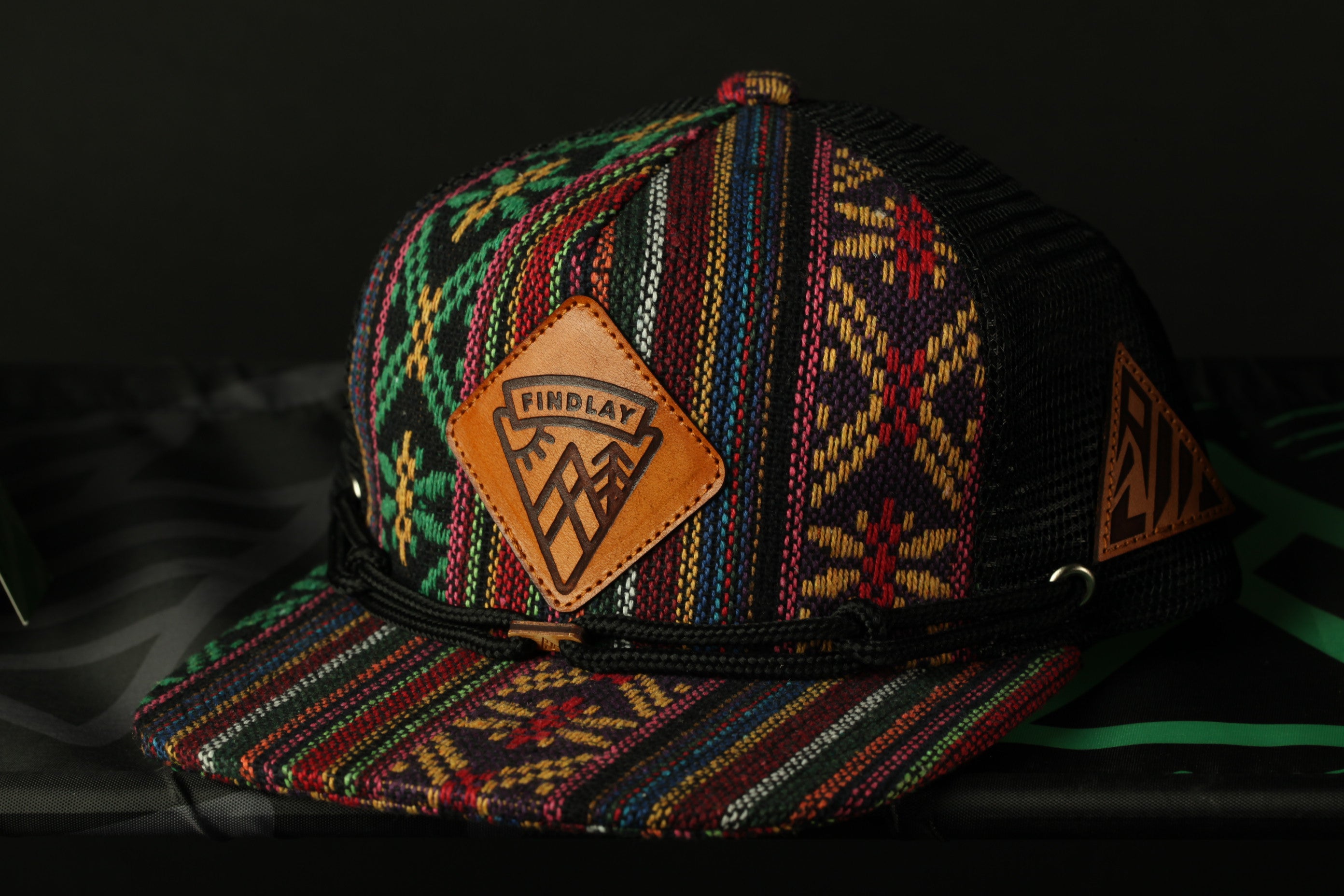A colorful, patterned baseball cap with a leather patch on the front, featuring a mountain design.